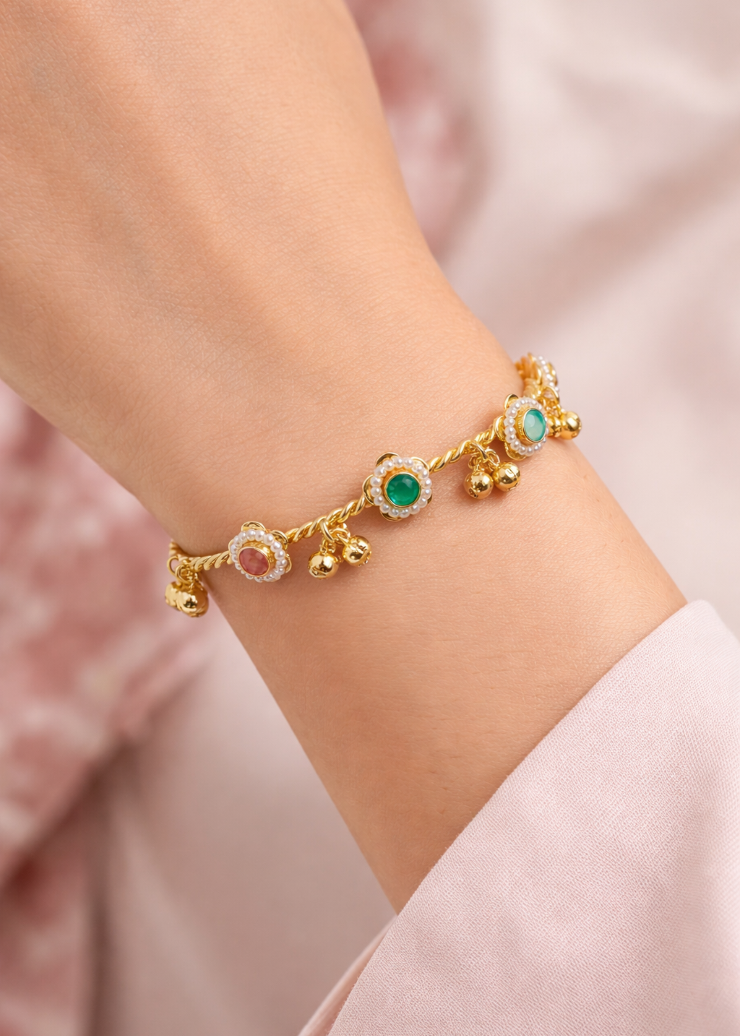 Gold bracelet with gemstones on a wrist against a soft pink background