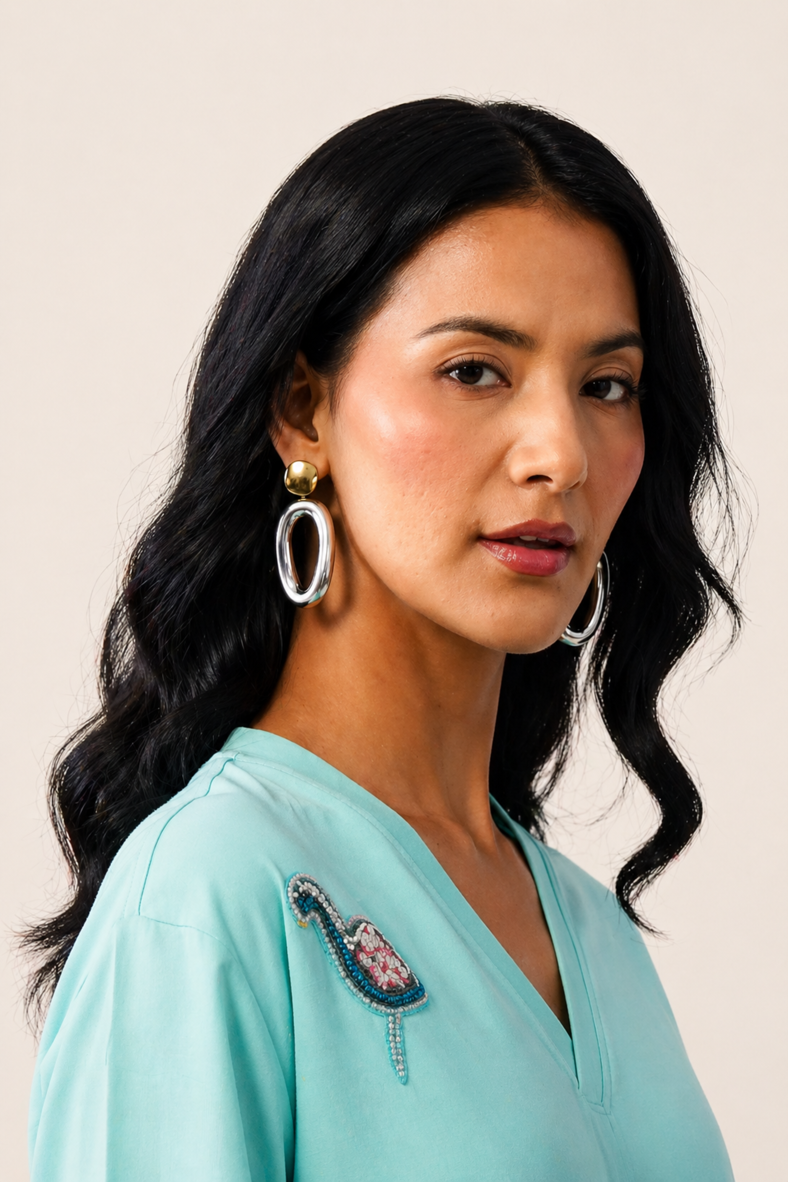 Woman wearing a light blue top with embroidery, posing against a neutral background