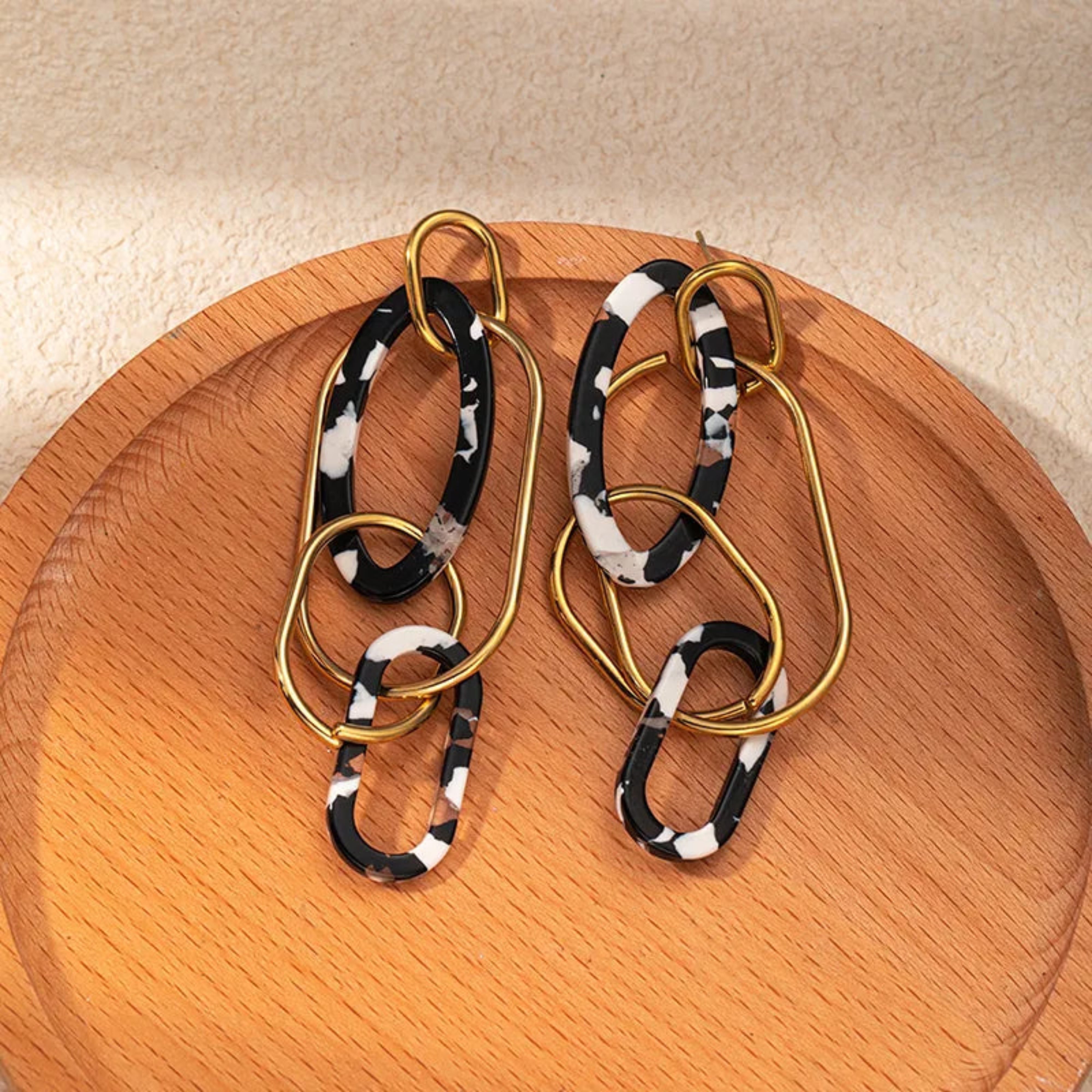 Pair of gold and black and white patterned earrings on a wooden surface