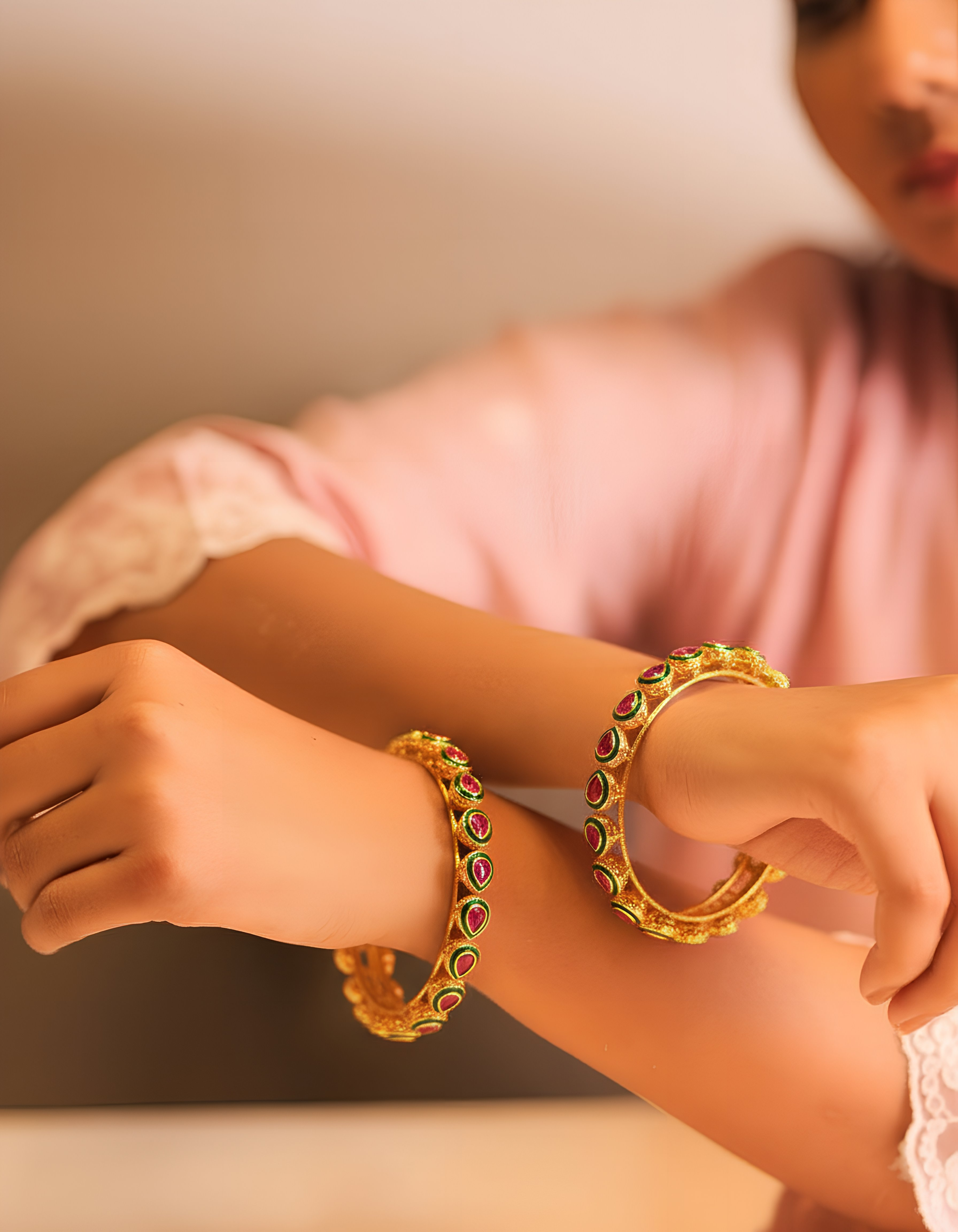 Gold bangles with colorful stones on a person's wrist against a neutral background