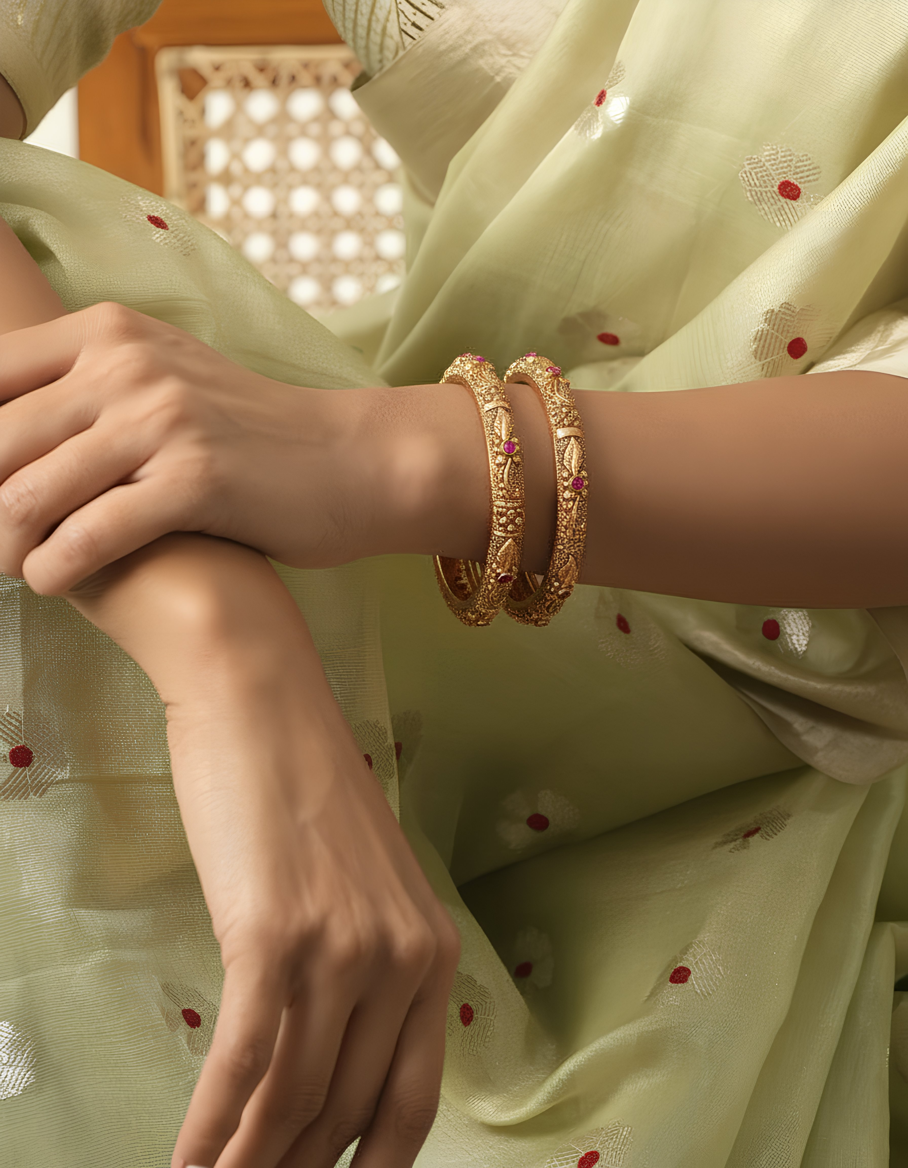 Close-up of a hand wearing a gold bracelet on a light green fabric background