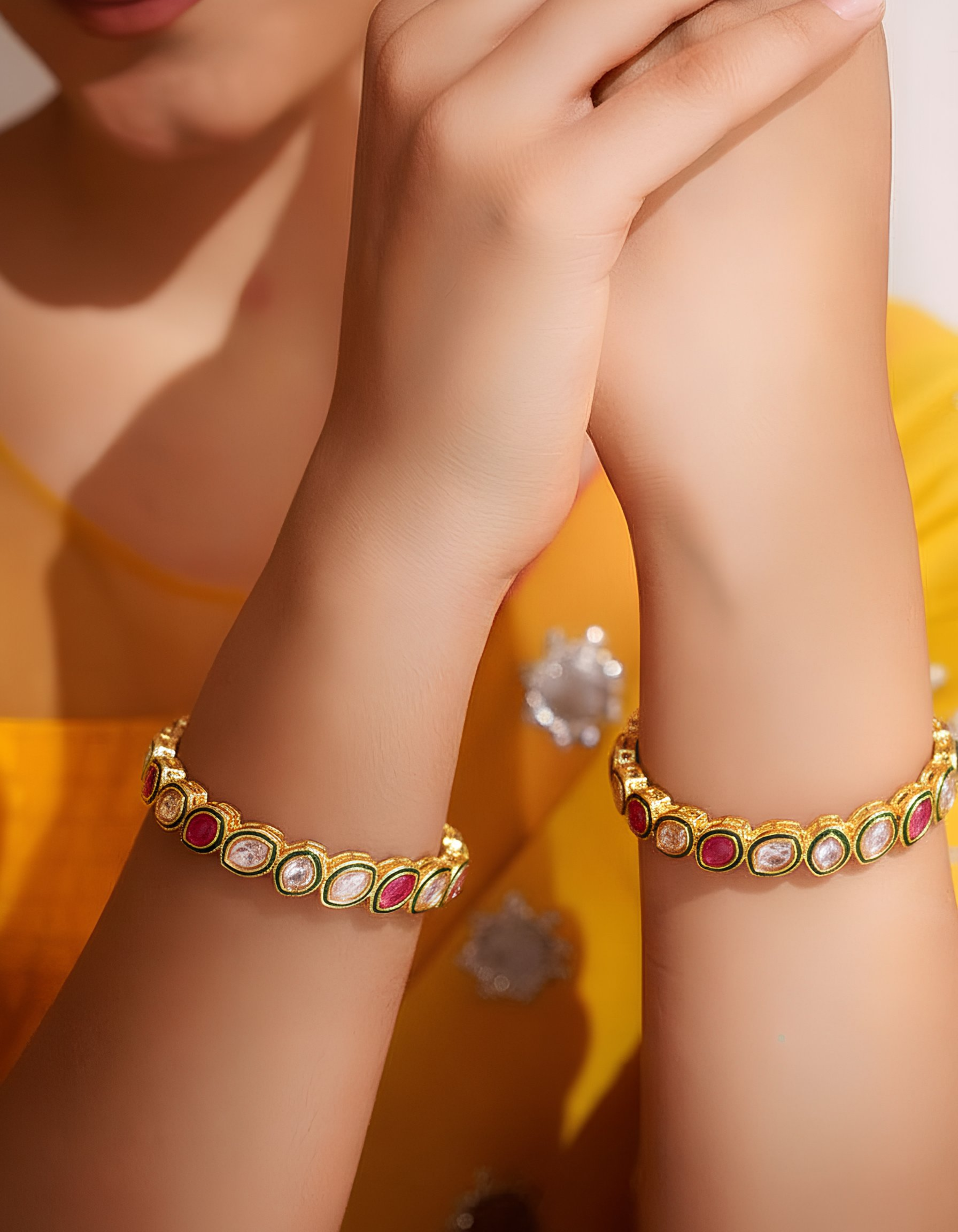 Gold bracelets with colorful stones on a person's wrist against a yellow background
