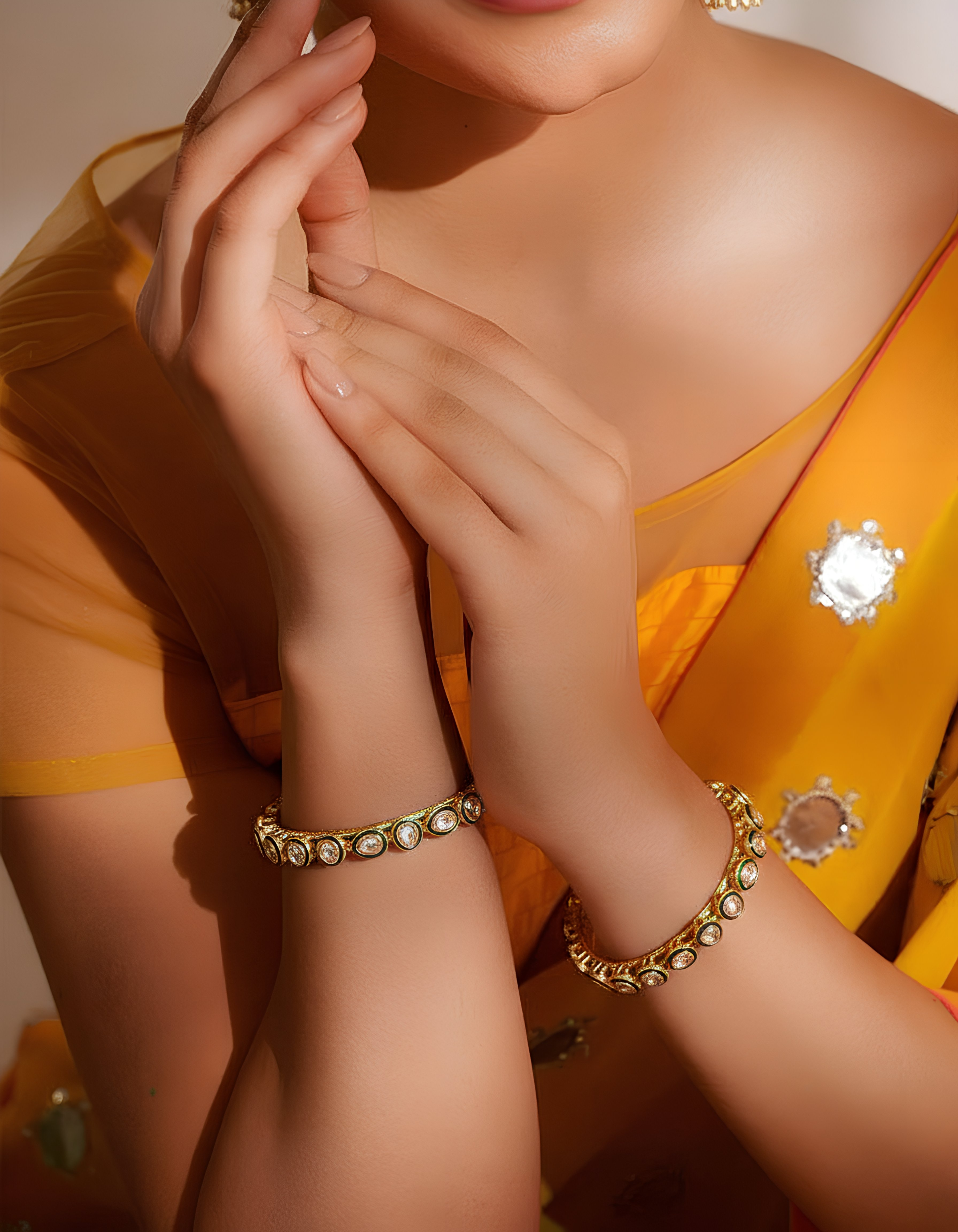 Close-up of a person wearing gold bracelets with a yellow saree in the background