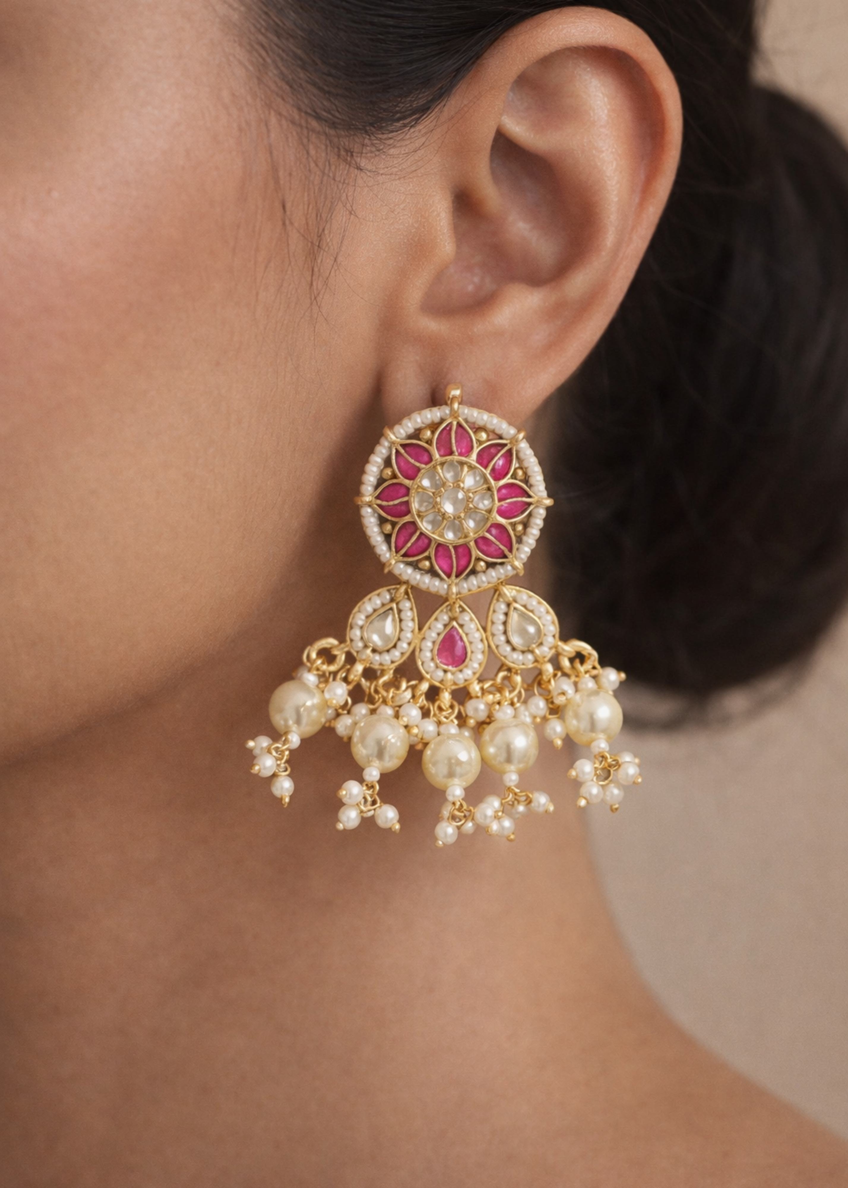 Close-up of a person wearing a decorative earring with pink gemstones and pearl drops.