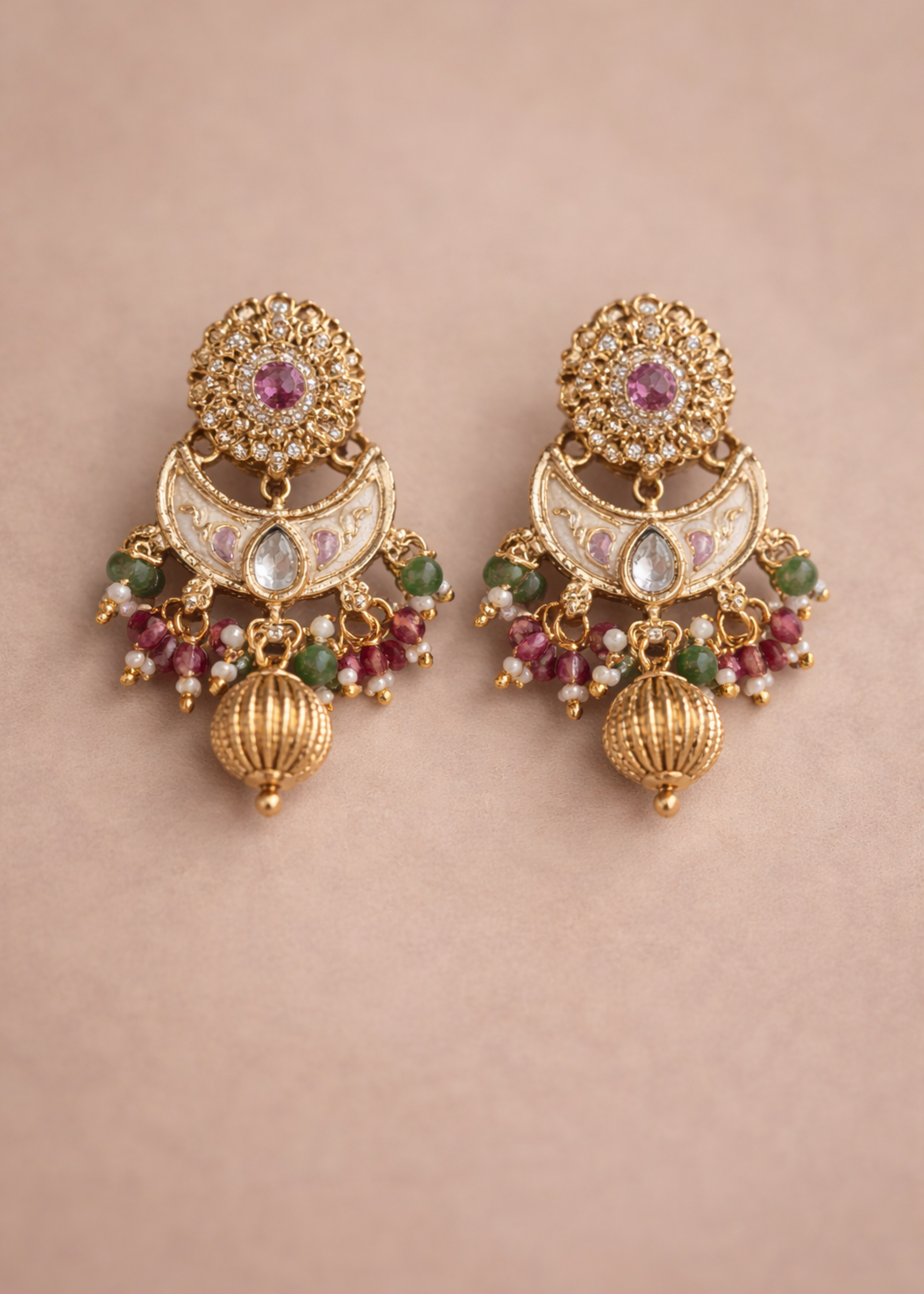 Ornate gold earrings with gemstones on a beige background