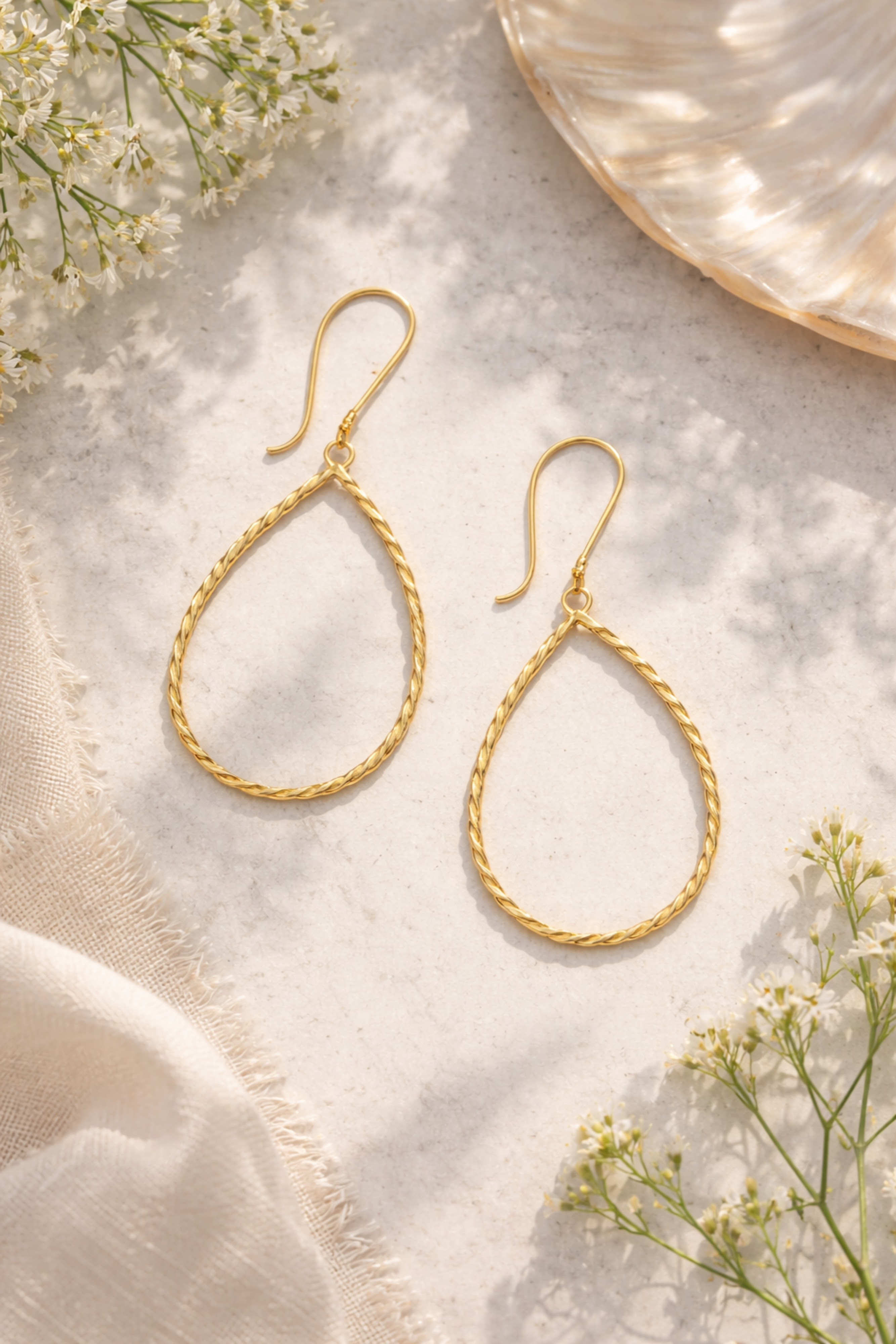 Gold teardrop earrings on a light background with flowers