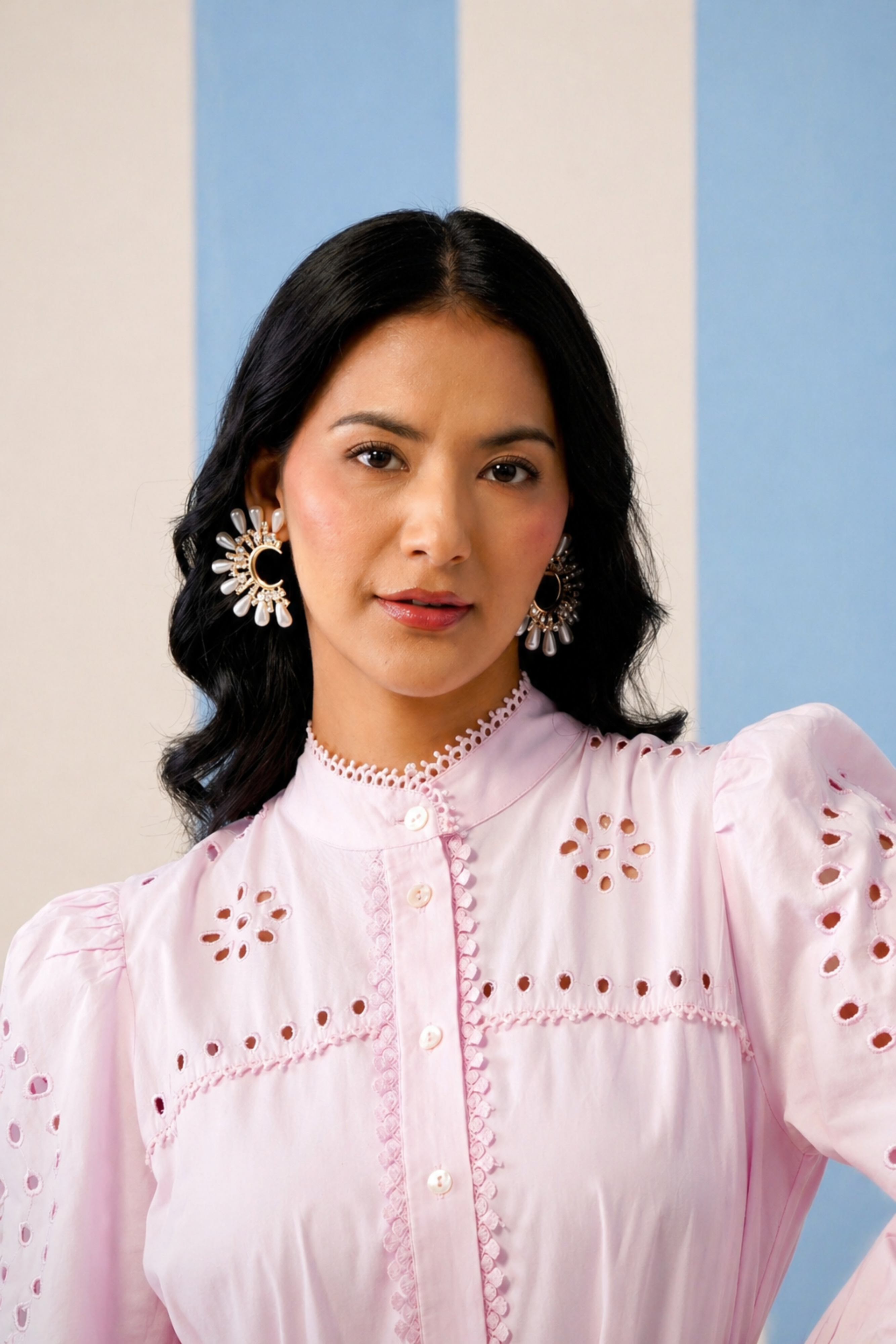 Woman wearing a pink blouse with intricate designs against a light blue and beige striped background
