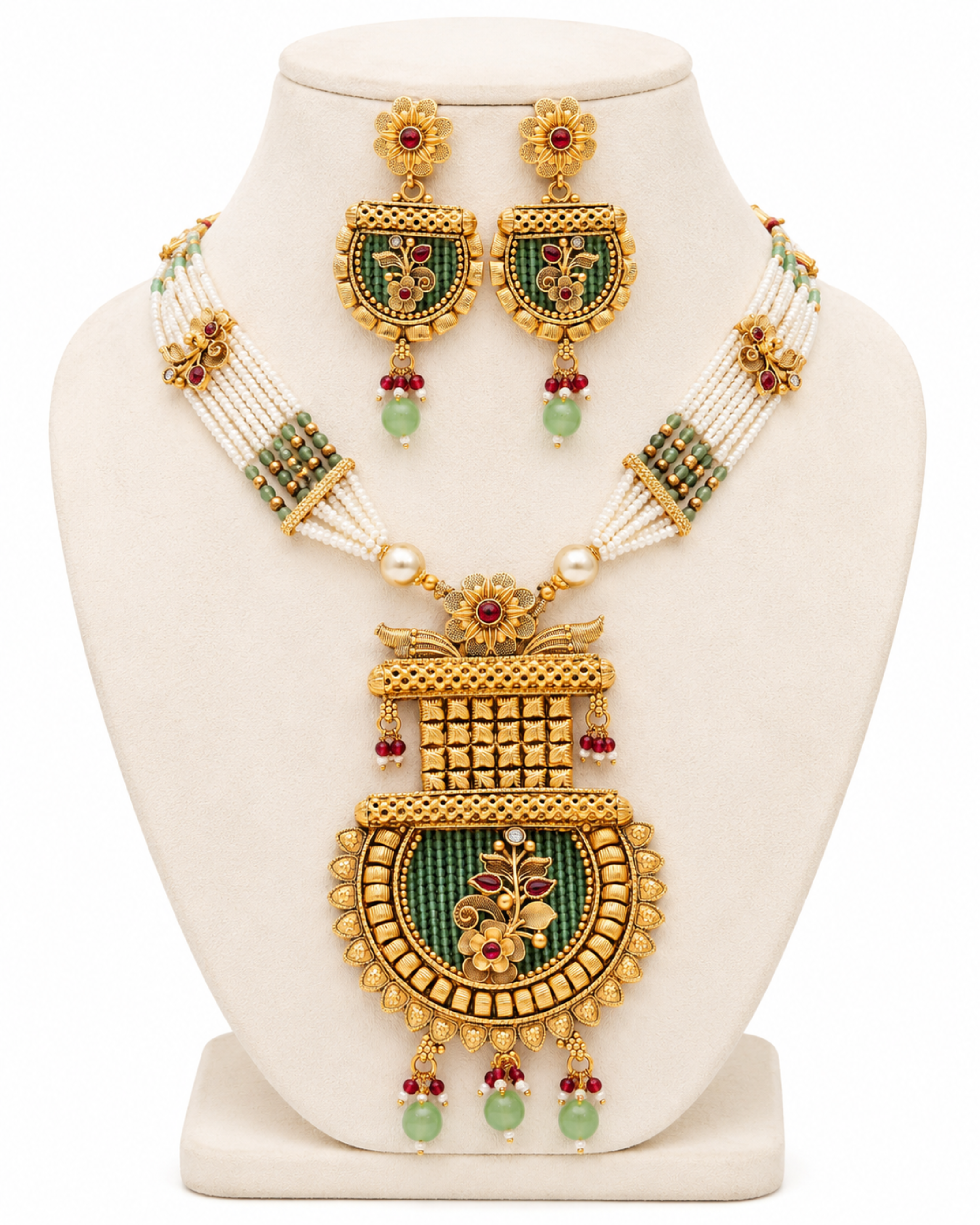 Ornate gold necklace with green stones and red beads on a white stand
