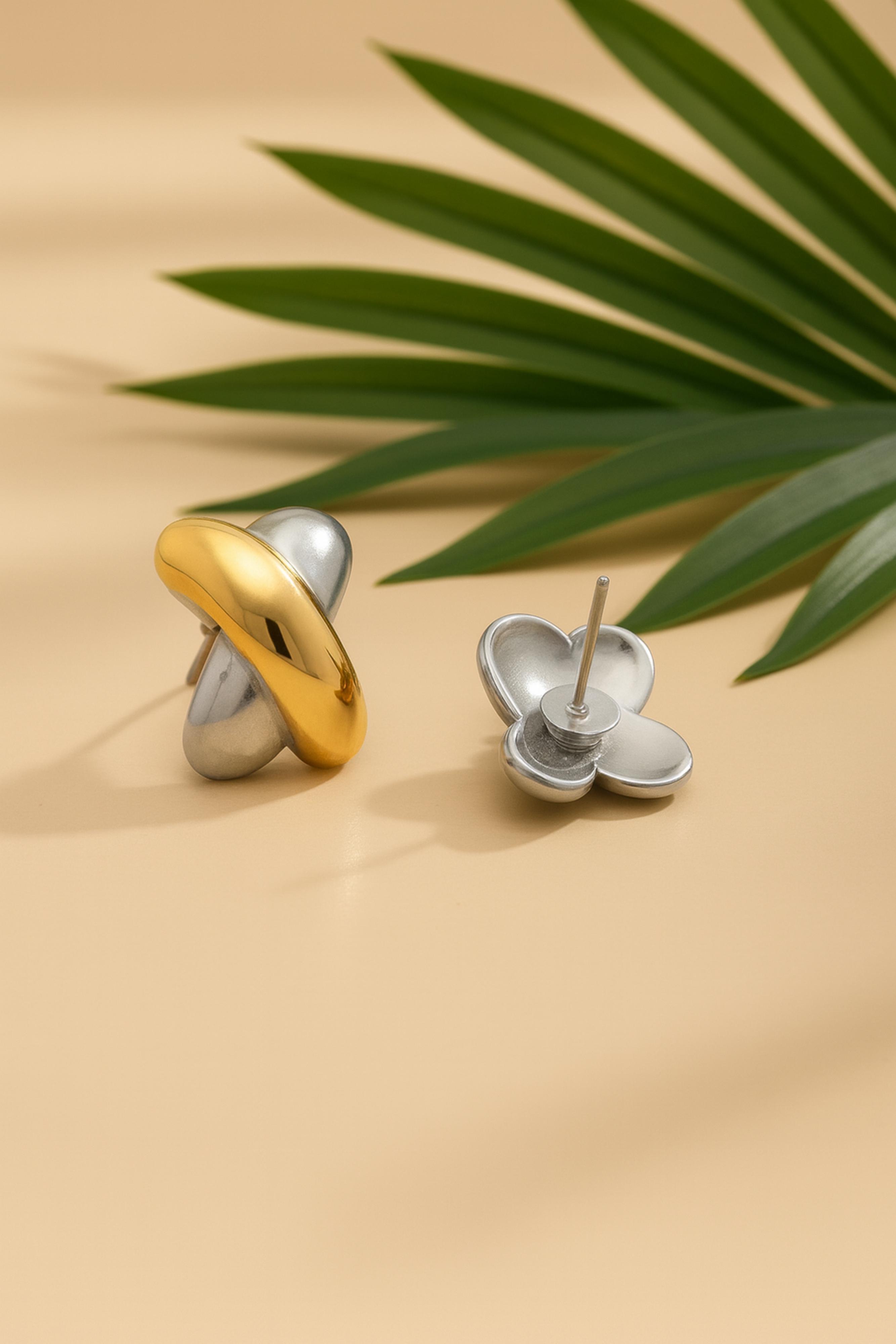 Gold and silver earrings on a beige surface with green leaves in the background