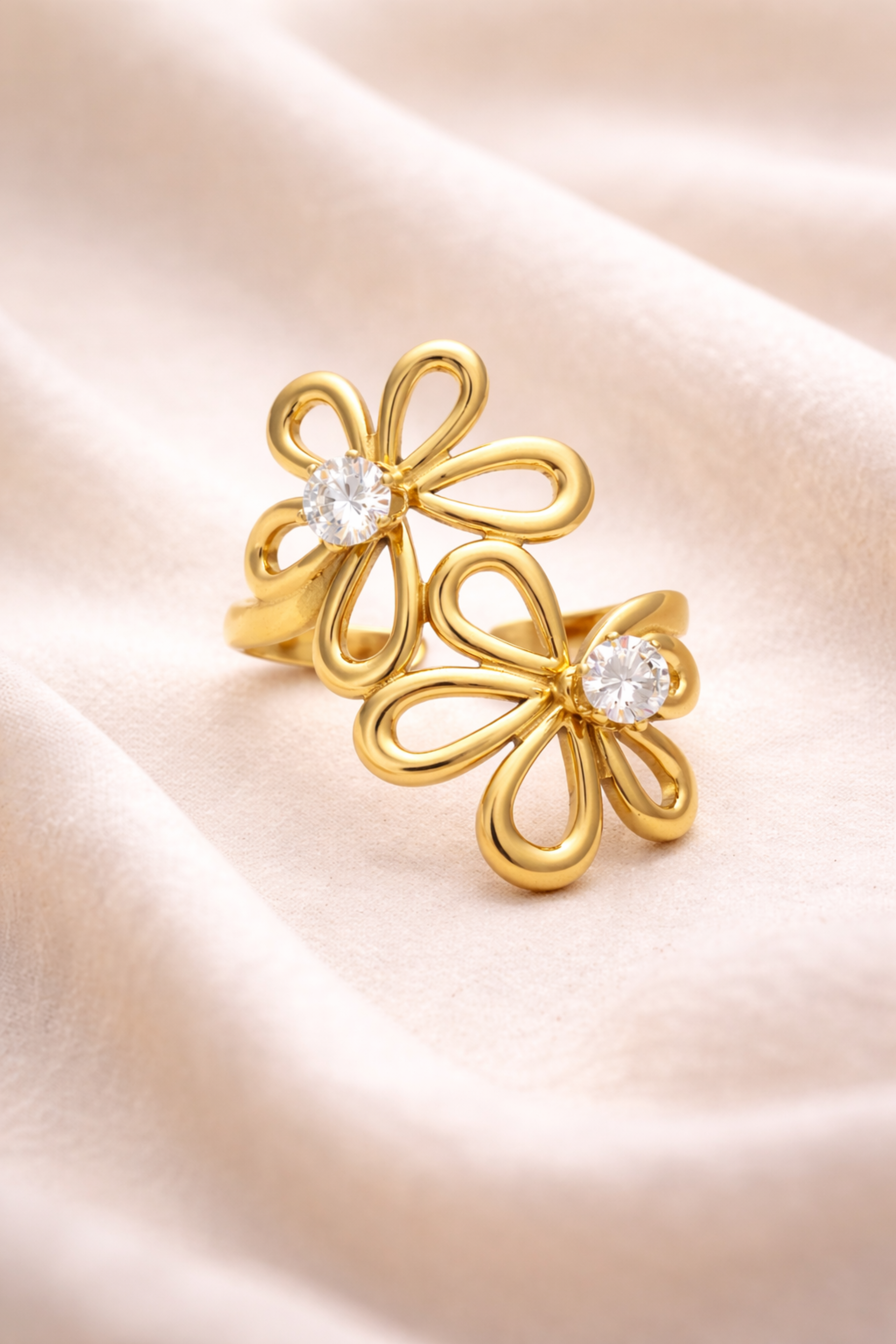 Gold flower-shaped earrings with clear stones on a soft pink fabric background