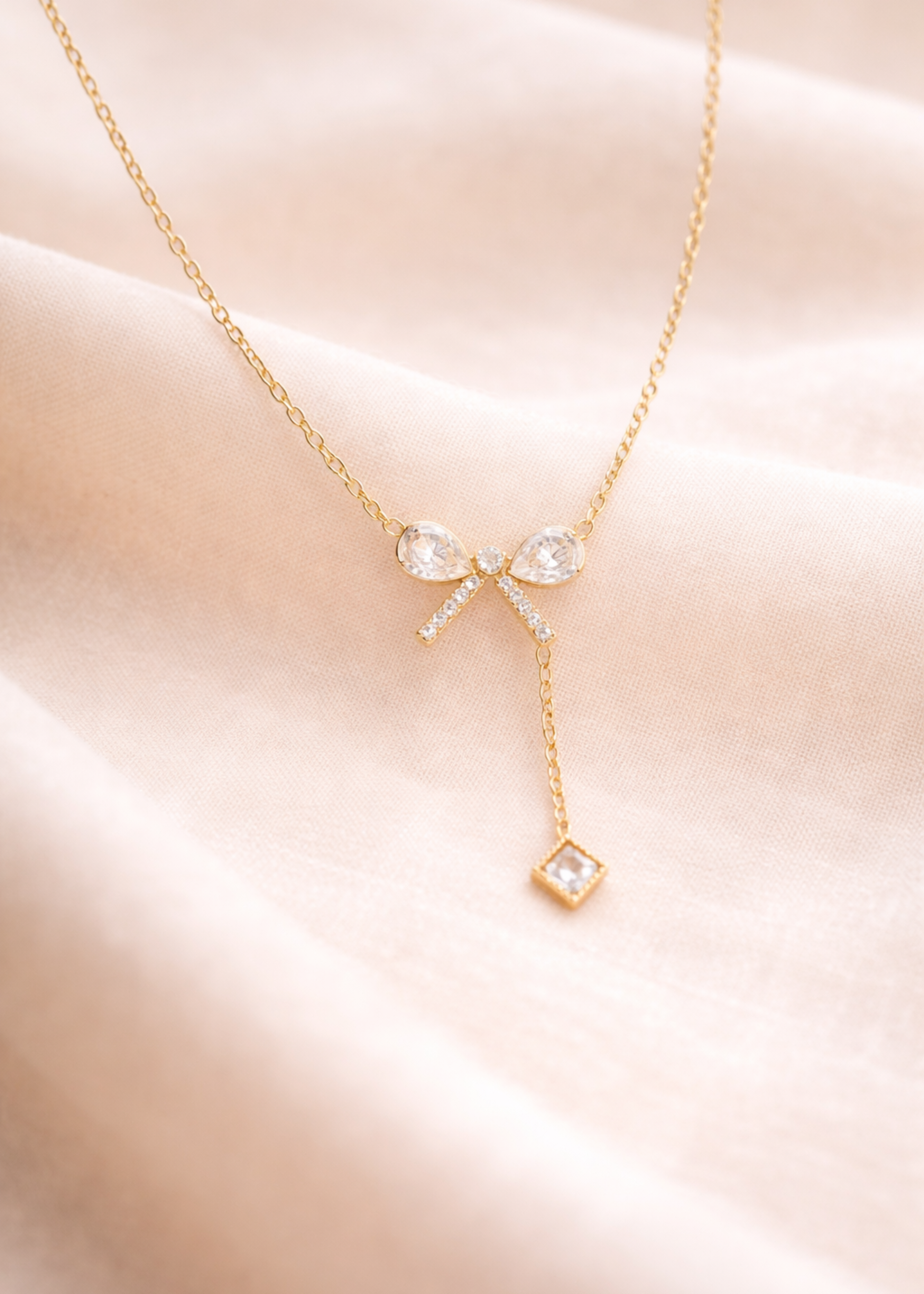 Gold necklace with bow and diamond pendants on a soft pink background