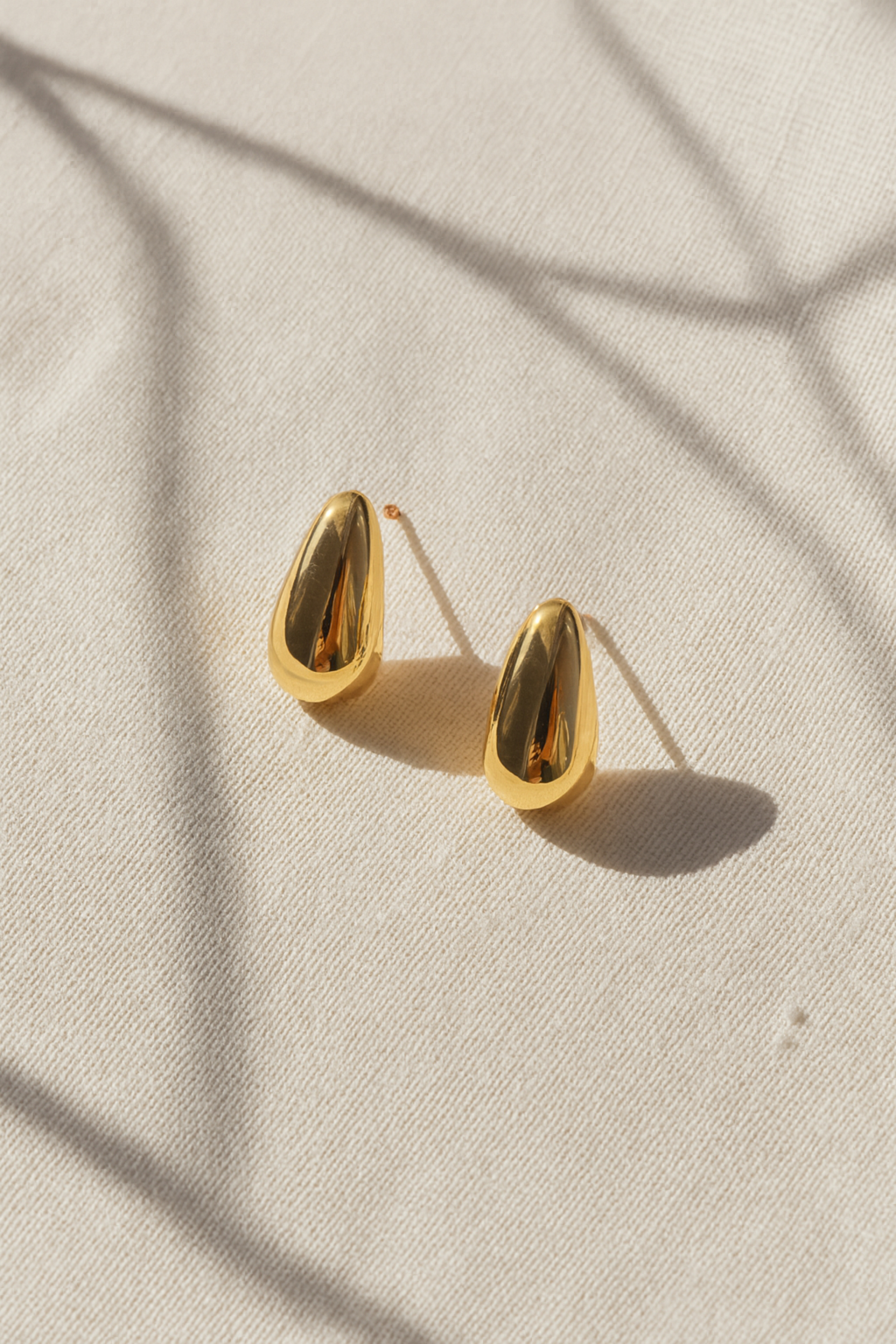 Gold teardrop earrings on a beige fabric background
