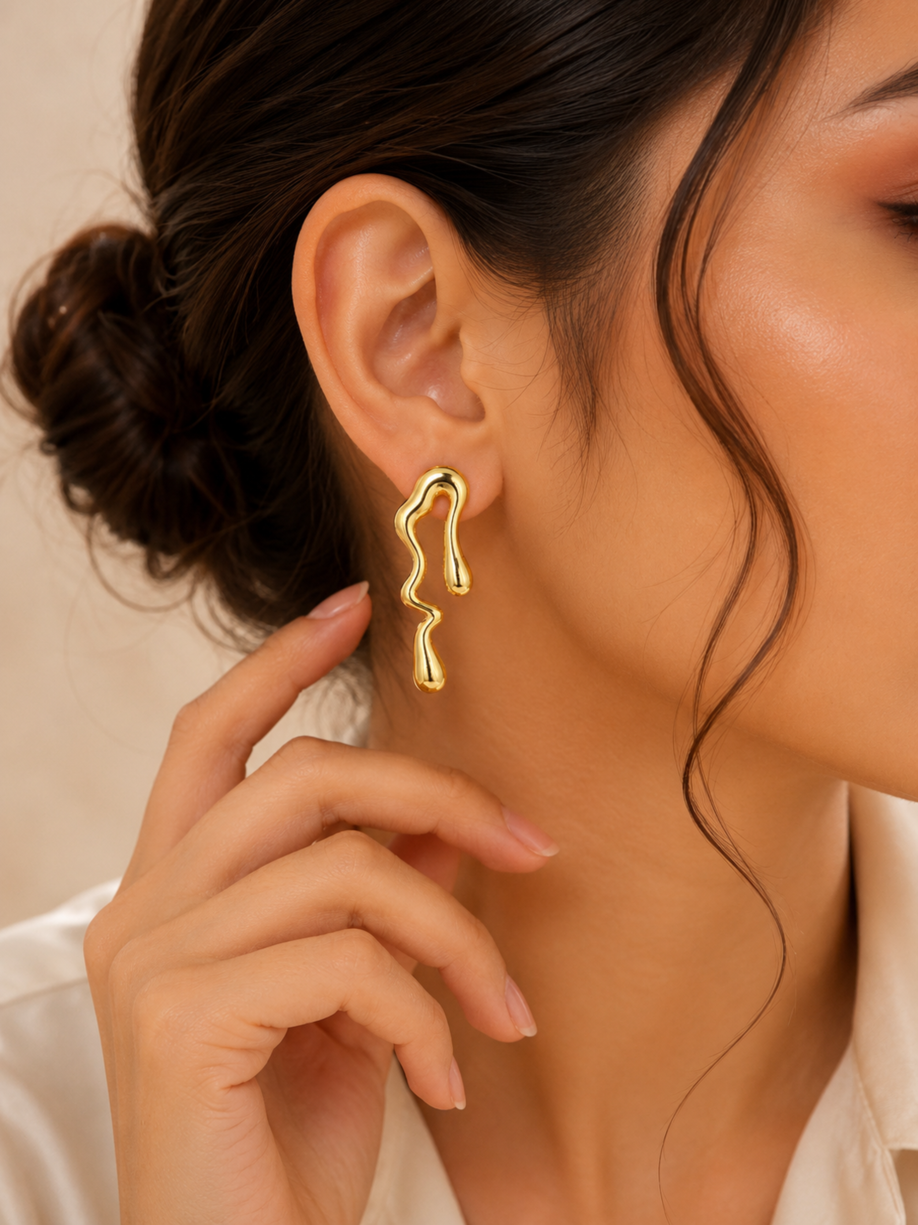 Gold earrings worn by a person with a neutral background