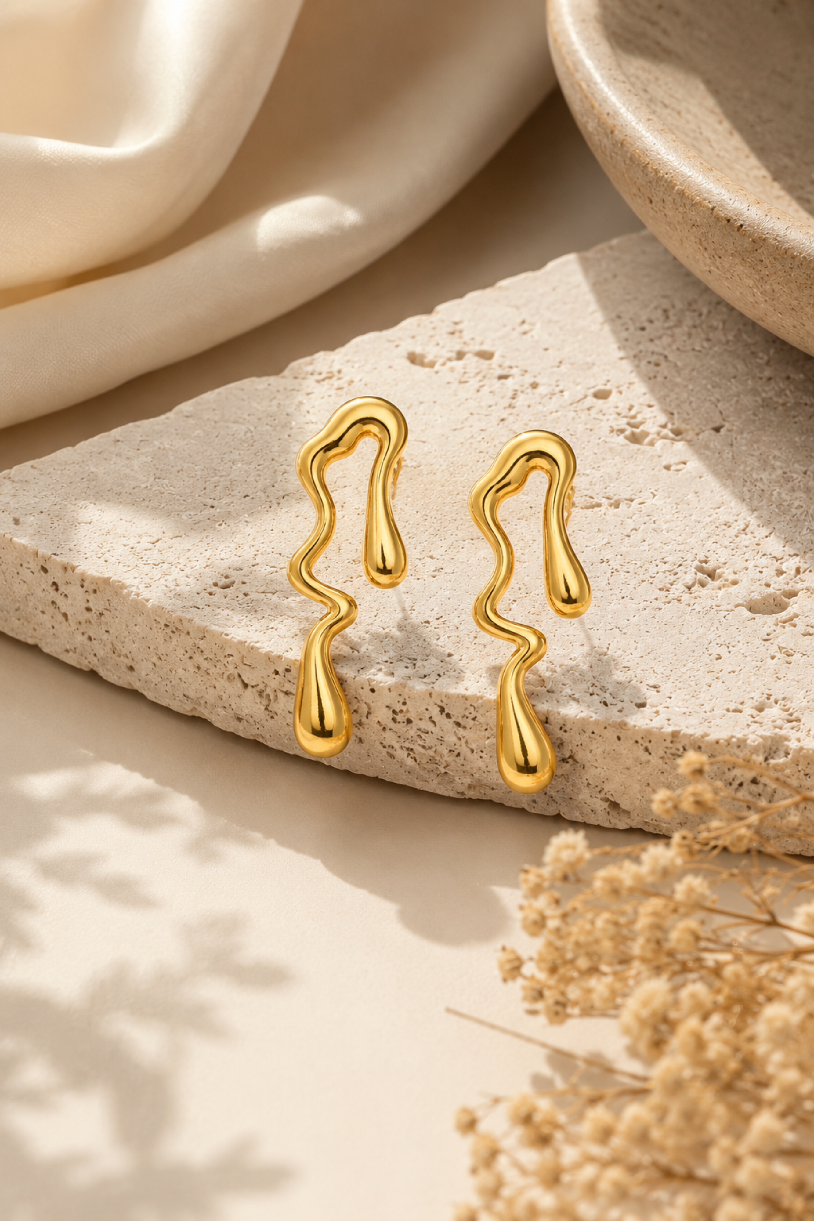 Gold earrings on a textured stone surface with a soft background
