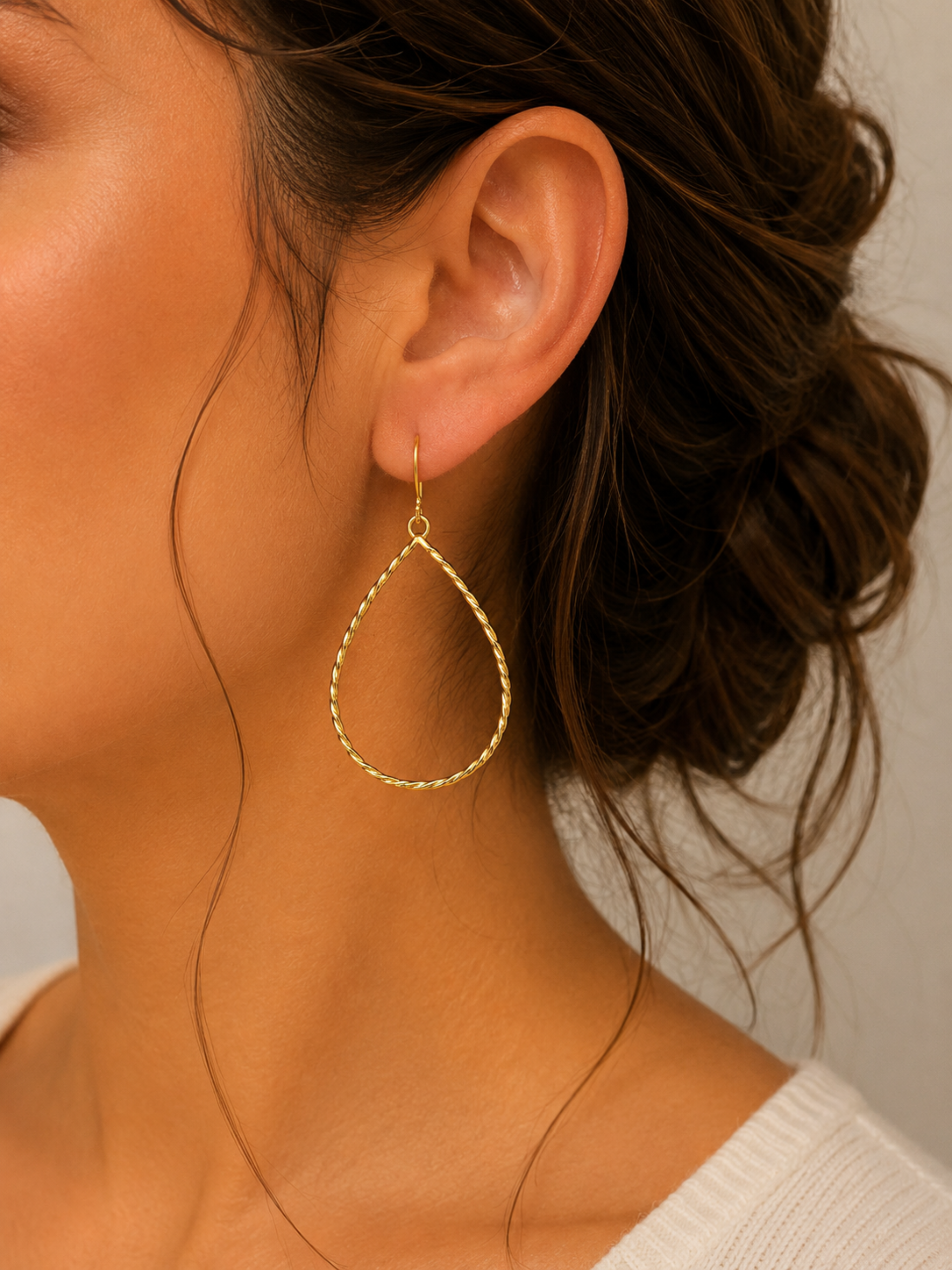 Close-up of a person wearing a gold hoop earring with a neutral background