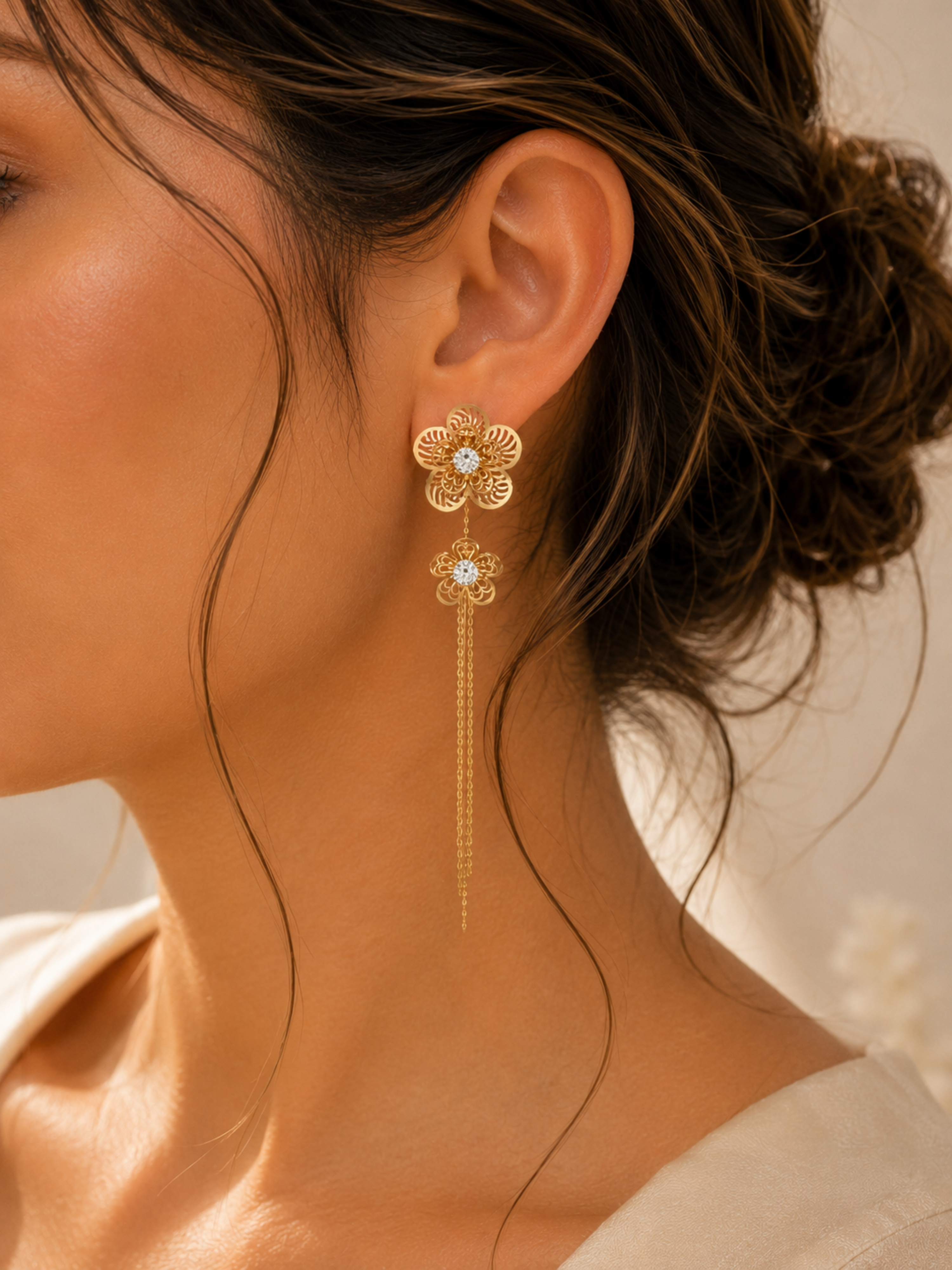 Gold floral earring with a long thread worn by a person with a blurred background