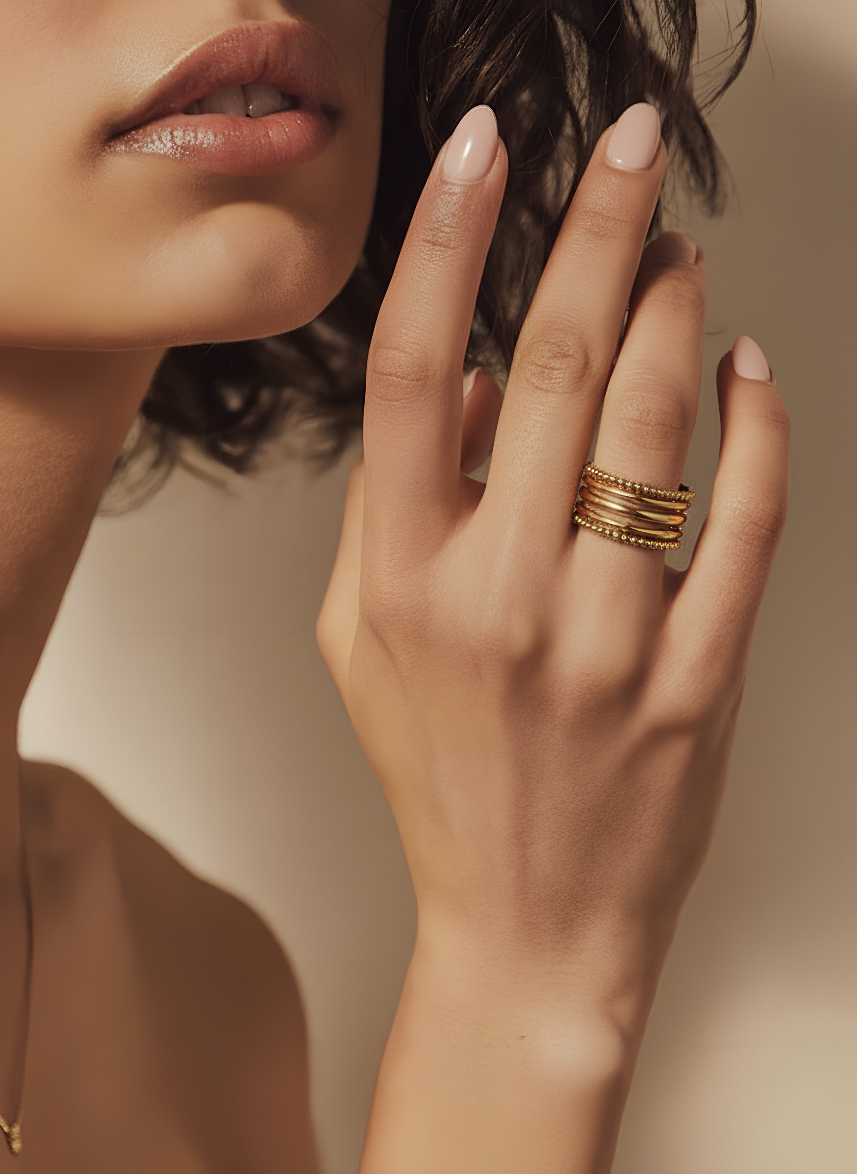 Close-up of a hand with multiple gold rings on a neutral background