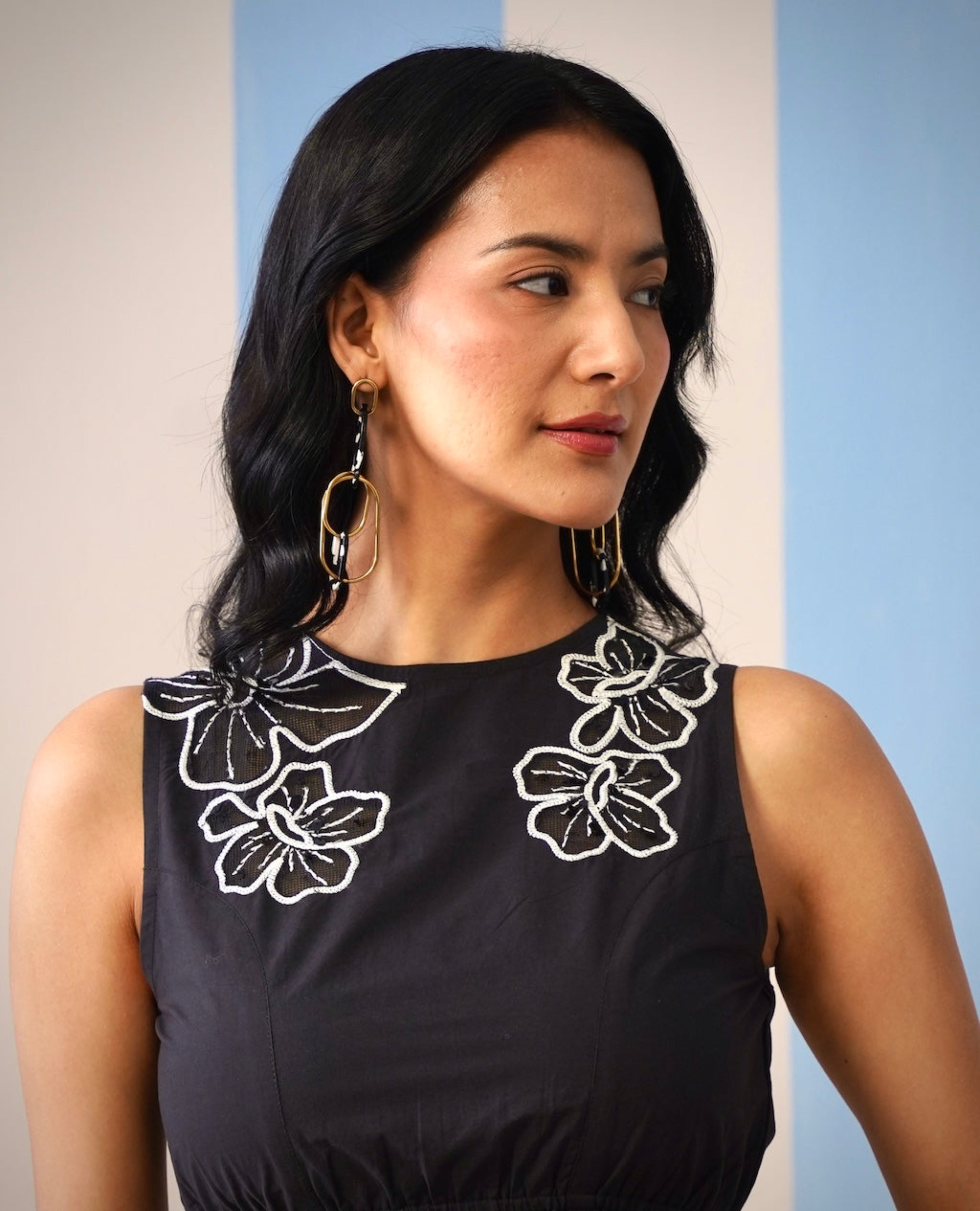 Woman wearing a black sleeveless top with white floral embroidery against a plain background