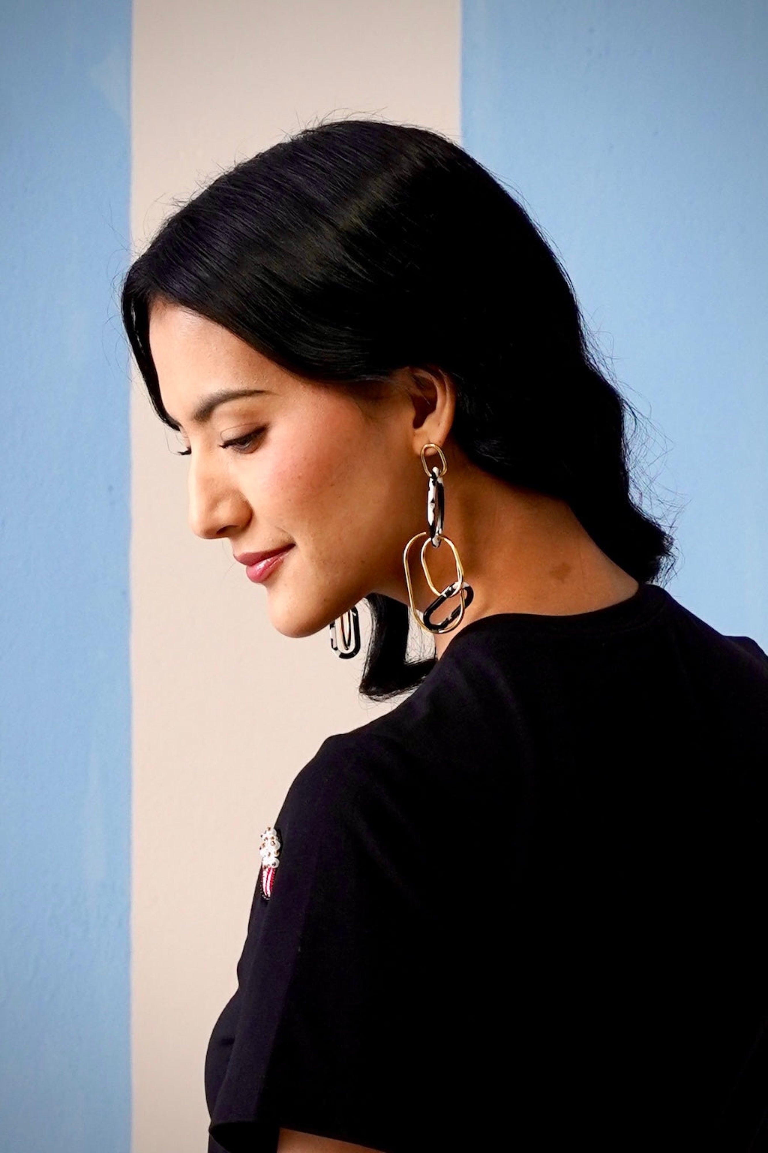 Woman wearing large hoop earrings against a light blue wall.