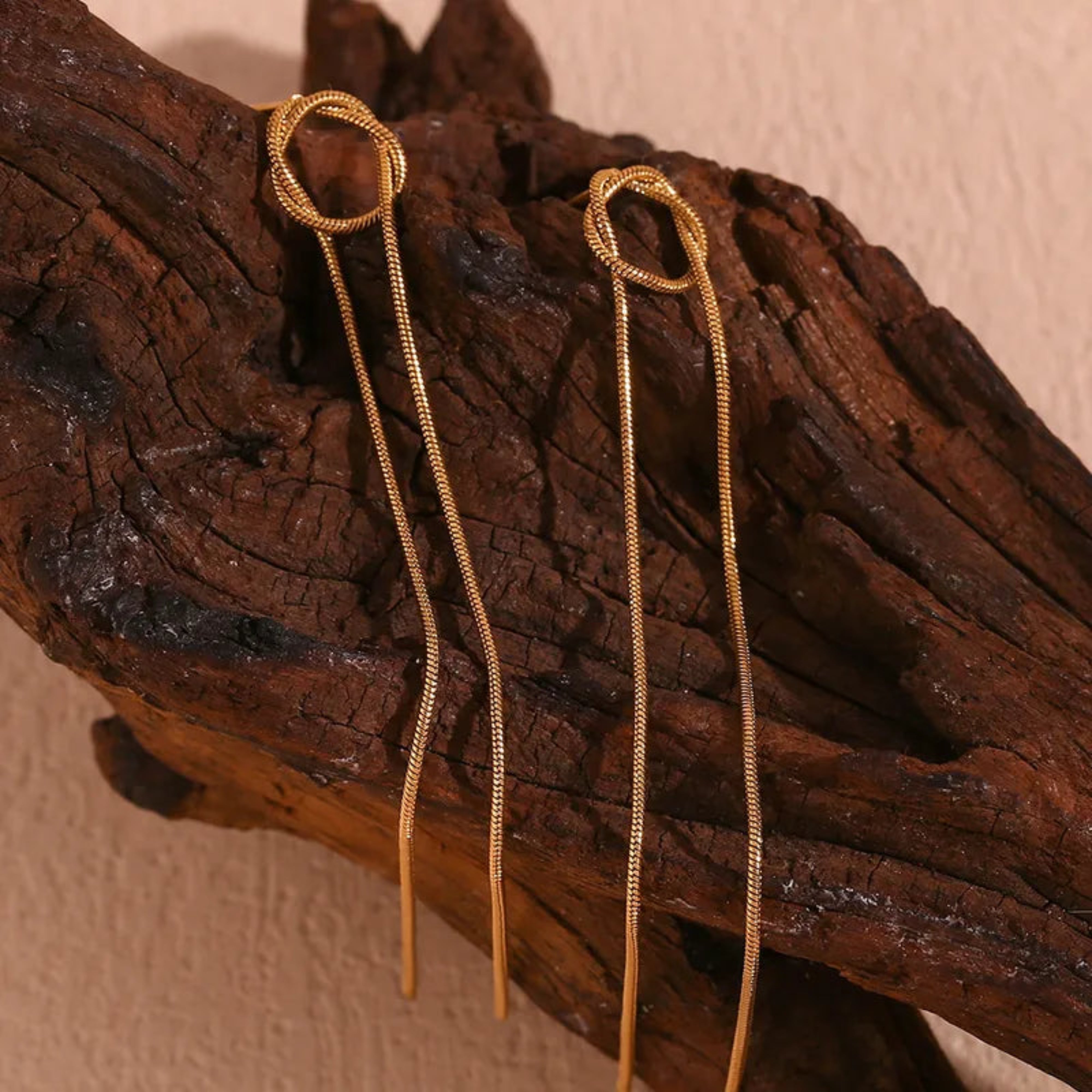 Gold snake chain earrings on a wooden surface