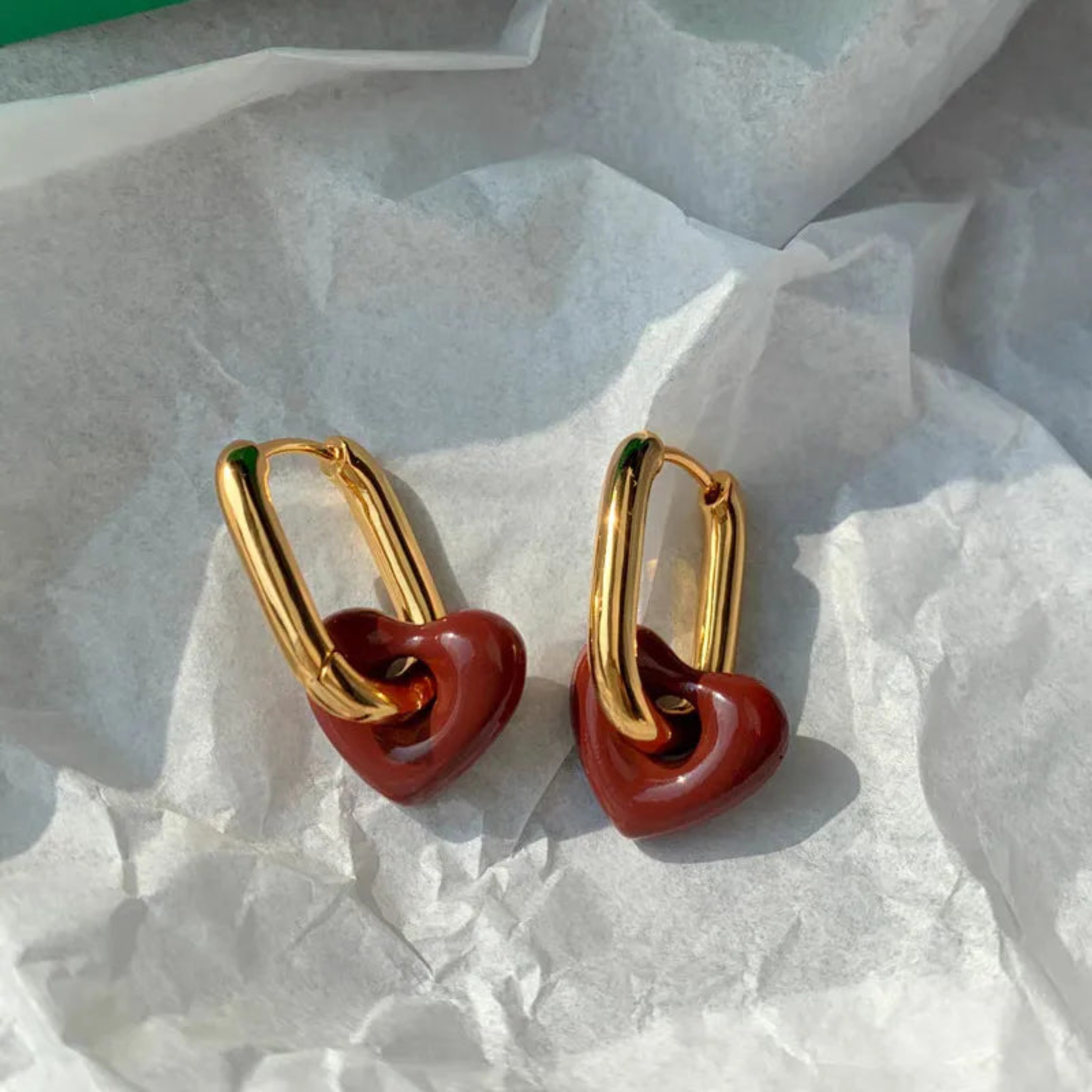 Gold heart-shaped earrings on a textured white surface