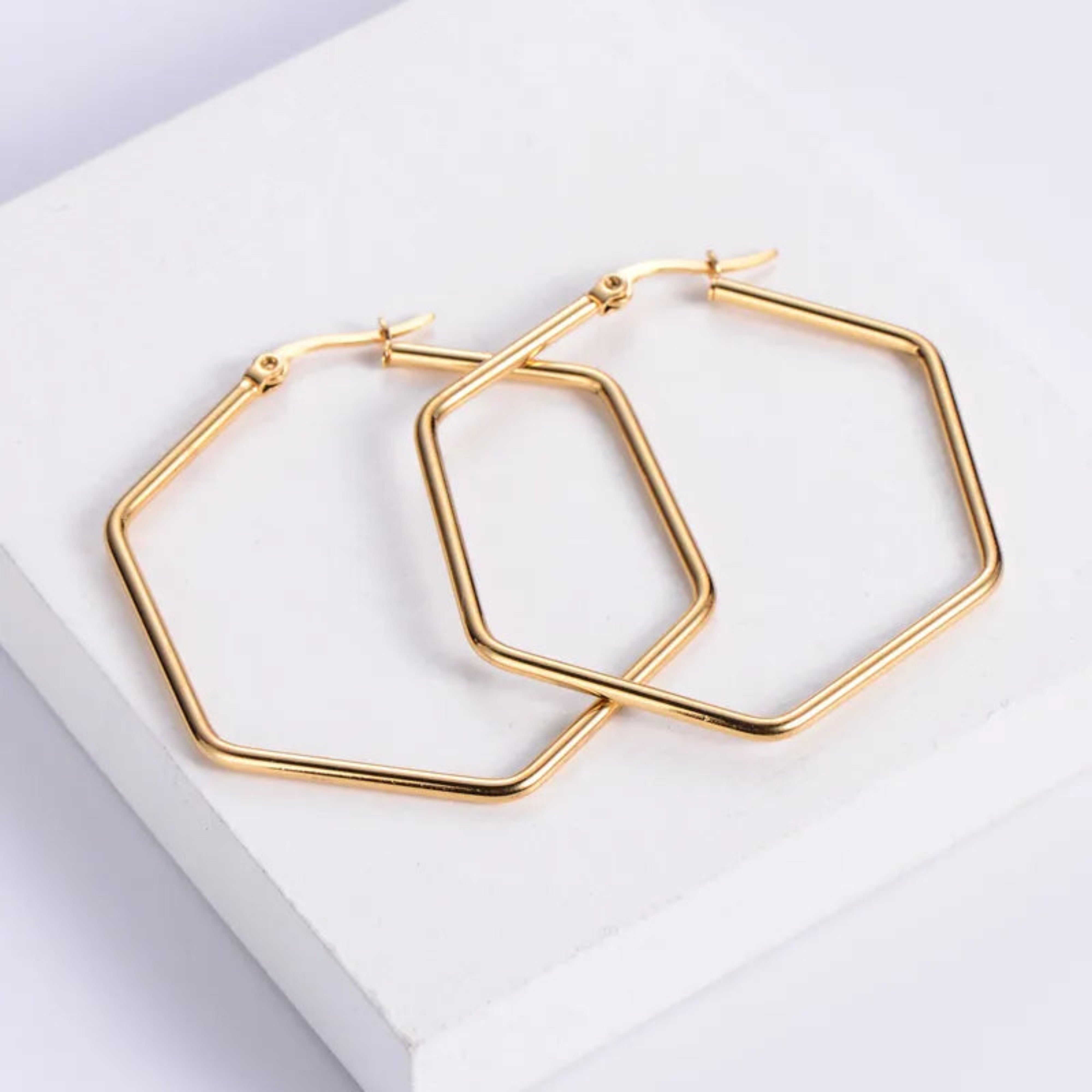 Gold hexagonal hoop earrings on a white surface