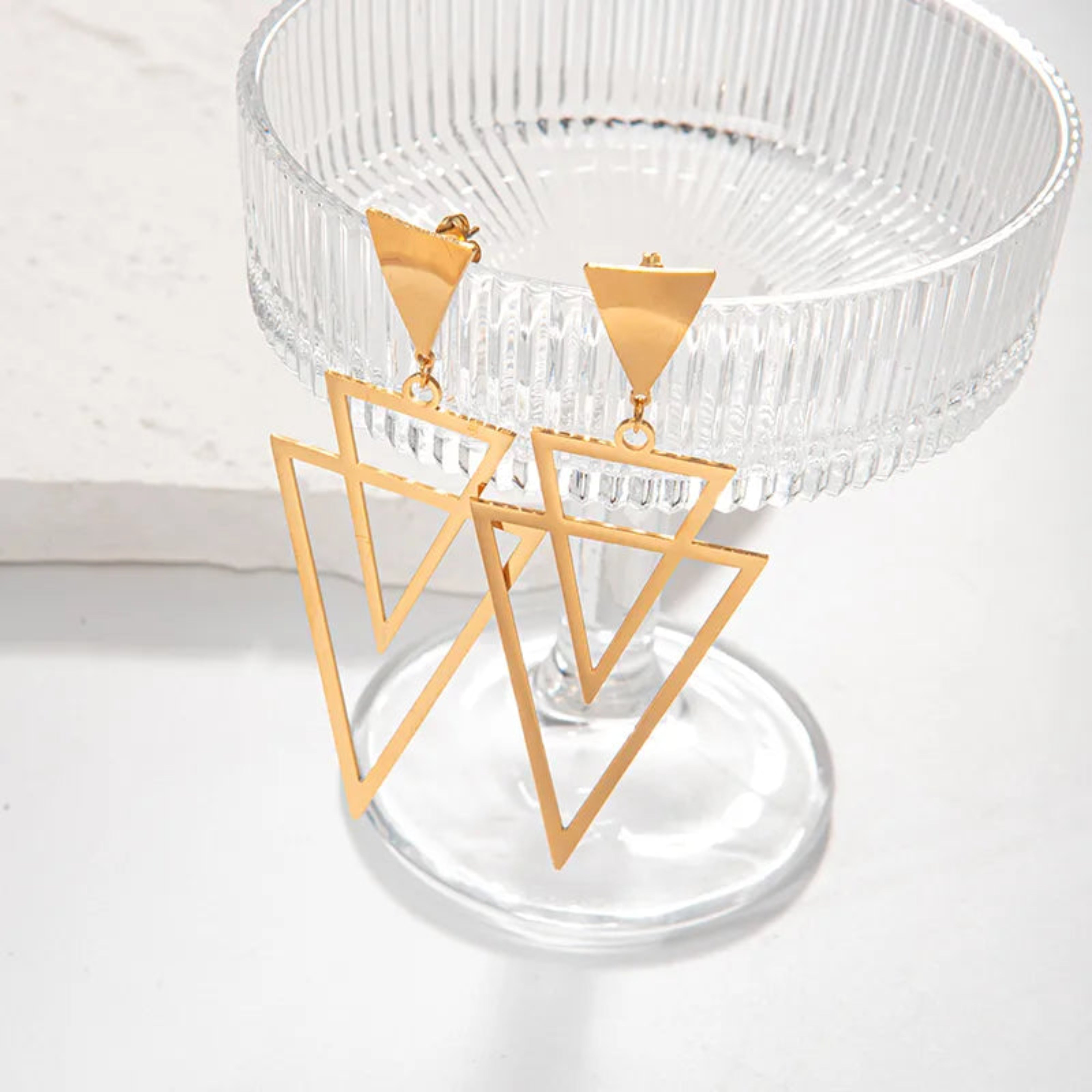 Gold triangle-shaped earrings on a clear stand with a white background