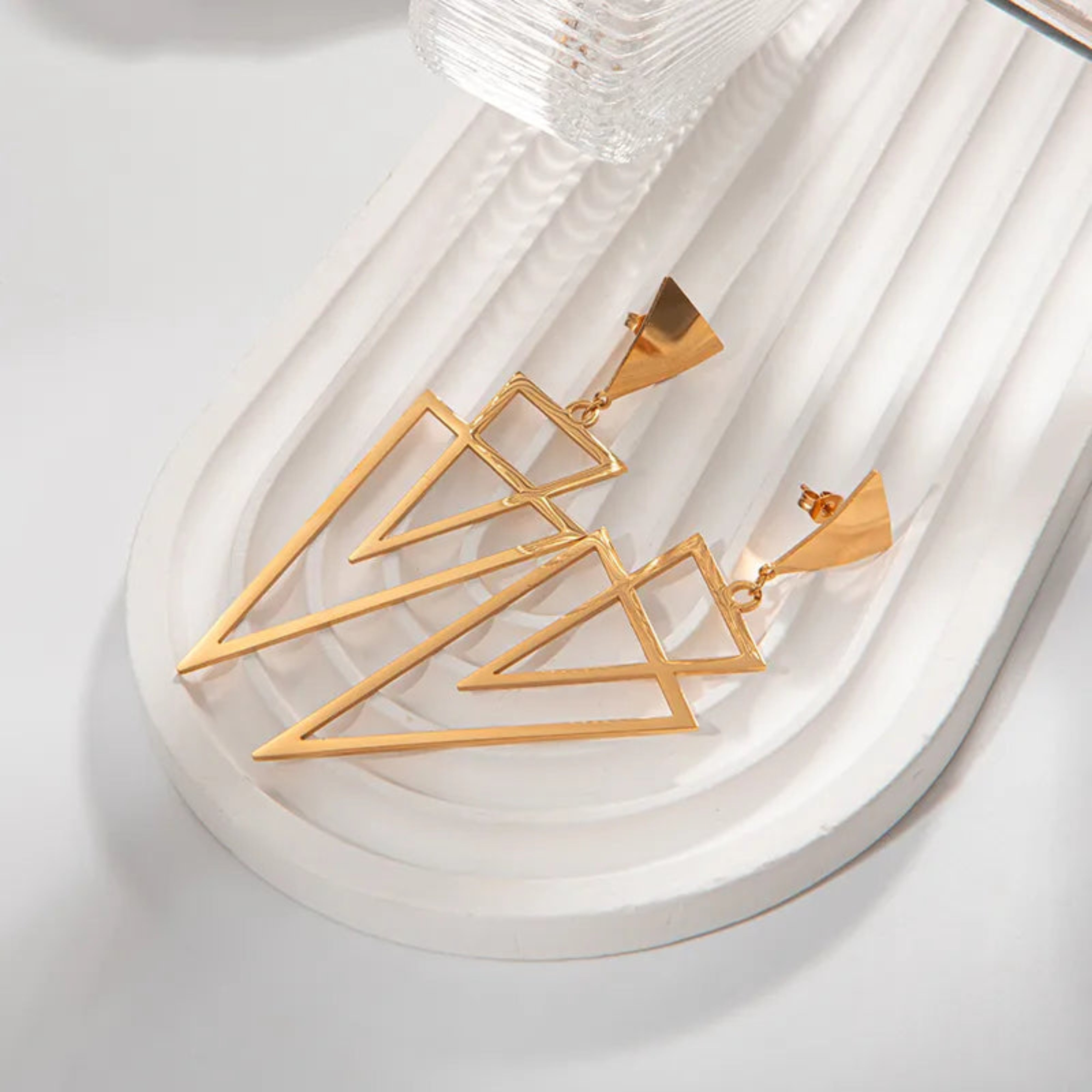 Gold geometric pendant on a white dish with a white background