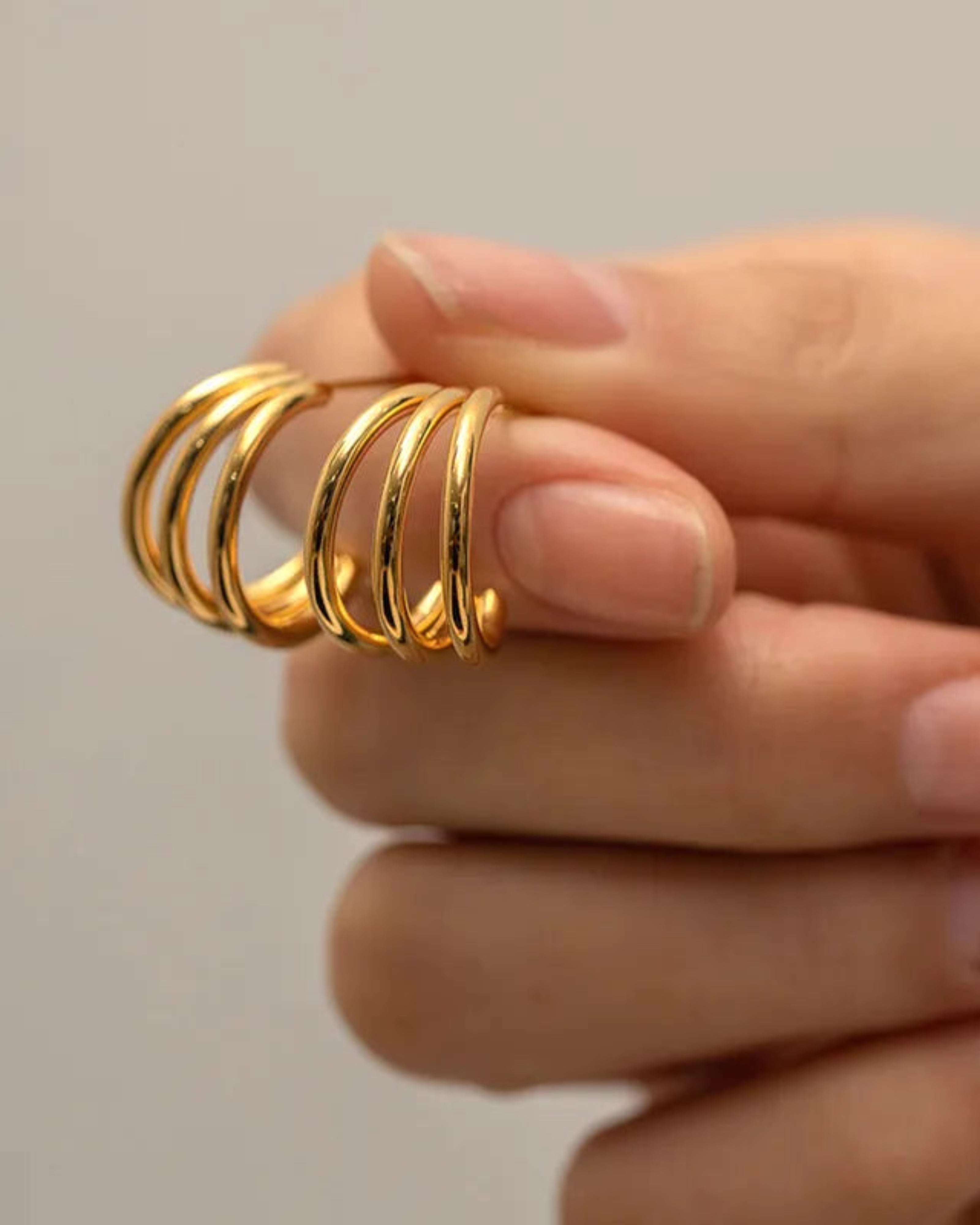 Gold spiral ring on a hand against a neutral background
