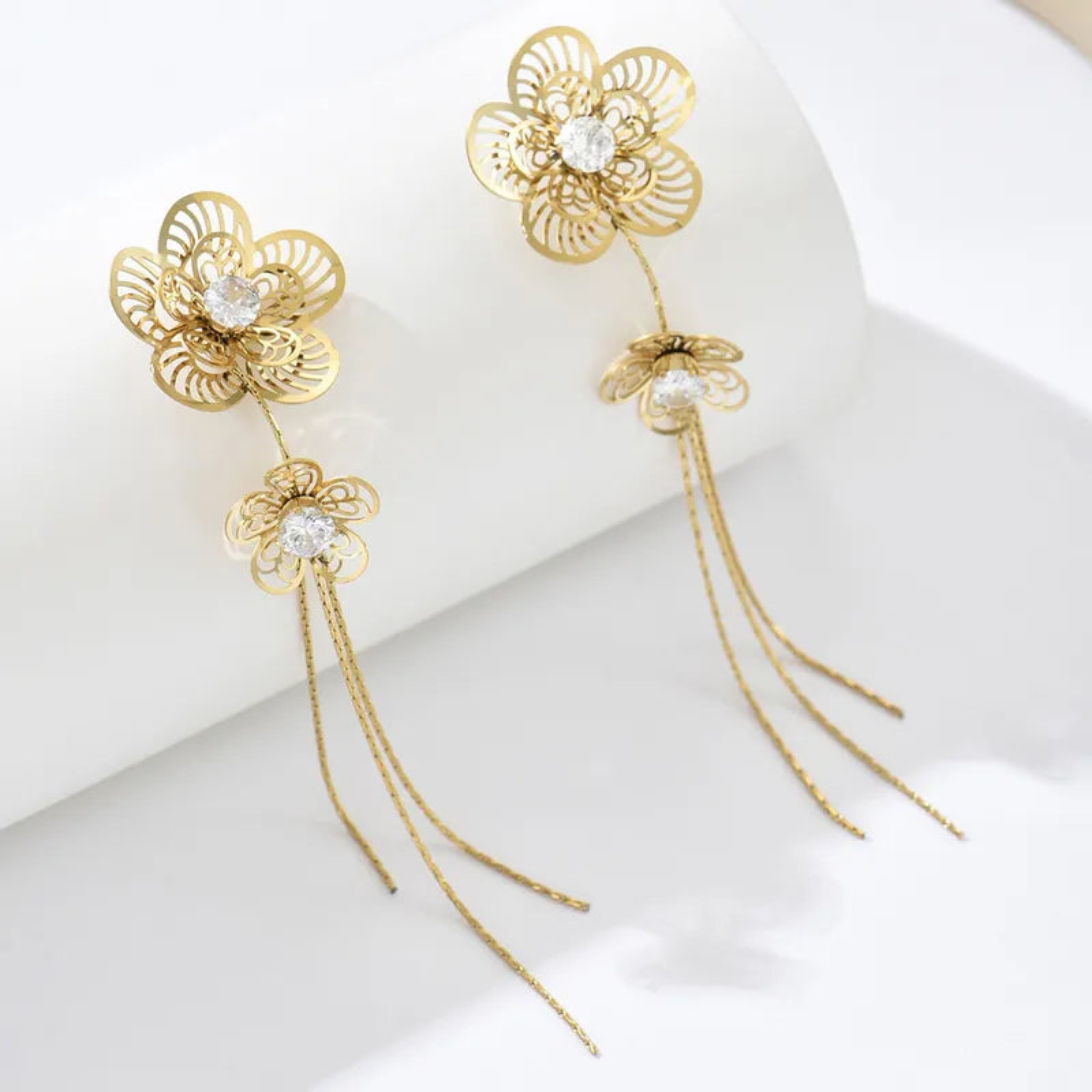 Gold floral earrings with tassels on a white background