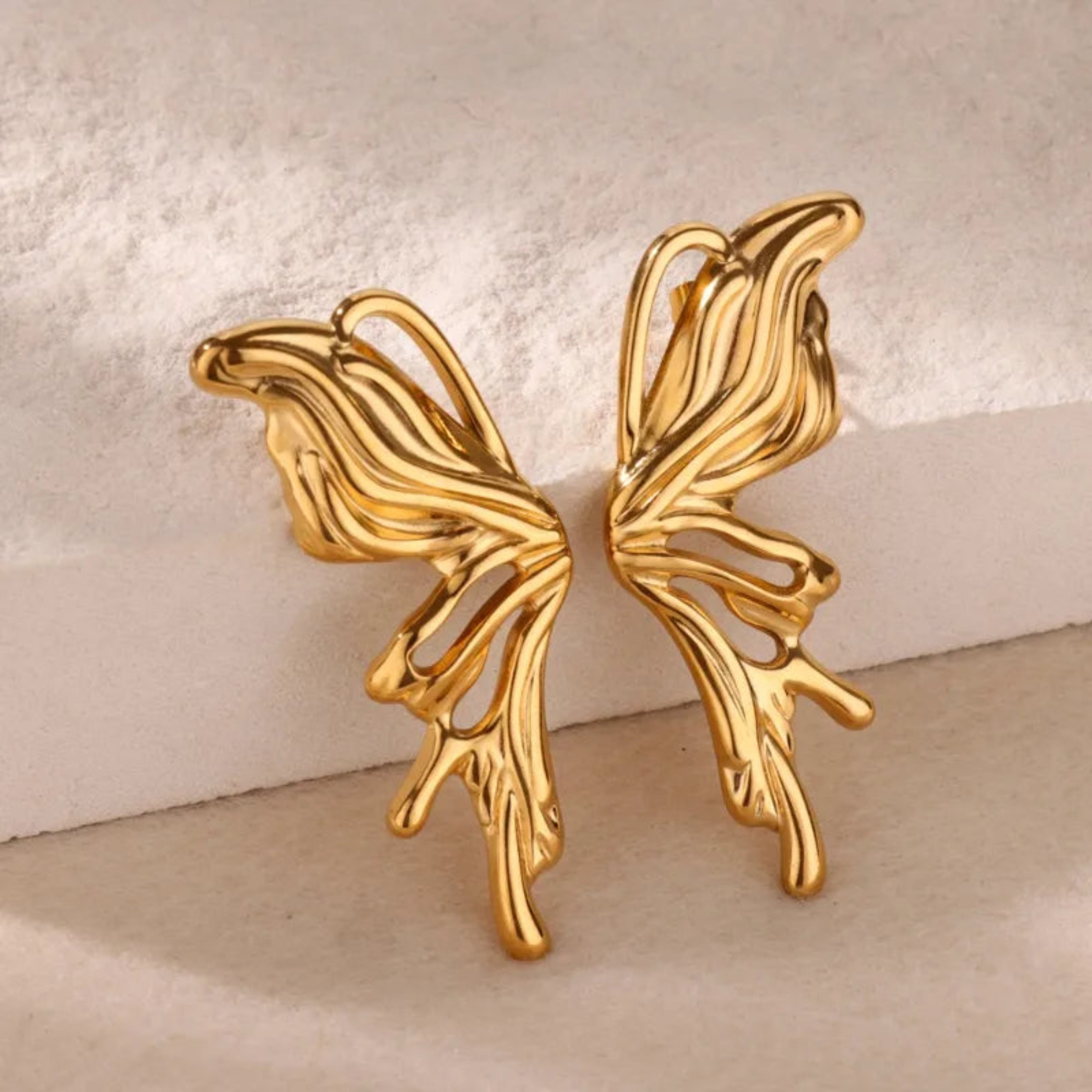 Gold butterfly-shaped earrings on a textured beige background