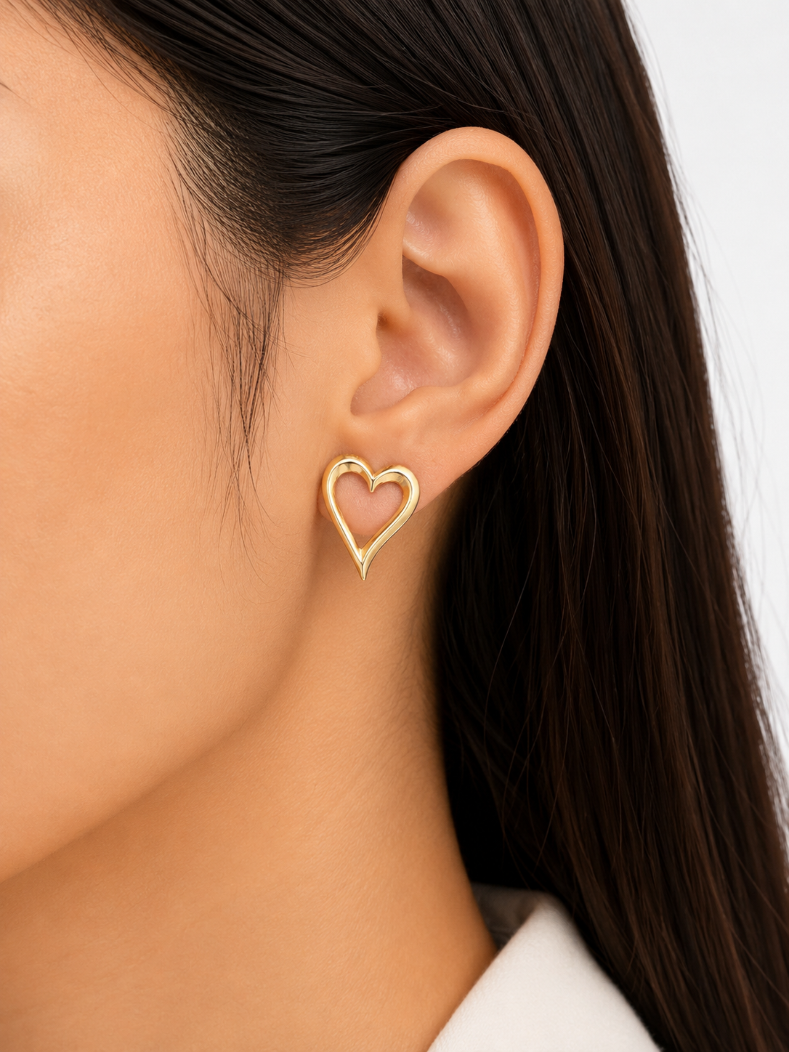 Gold heart-shaped earring worn by a person with dark hair.