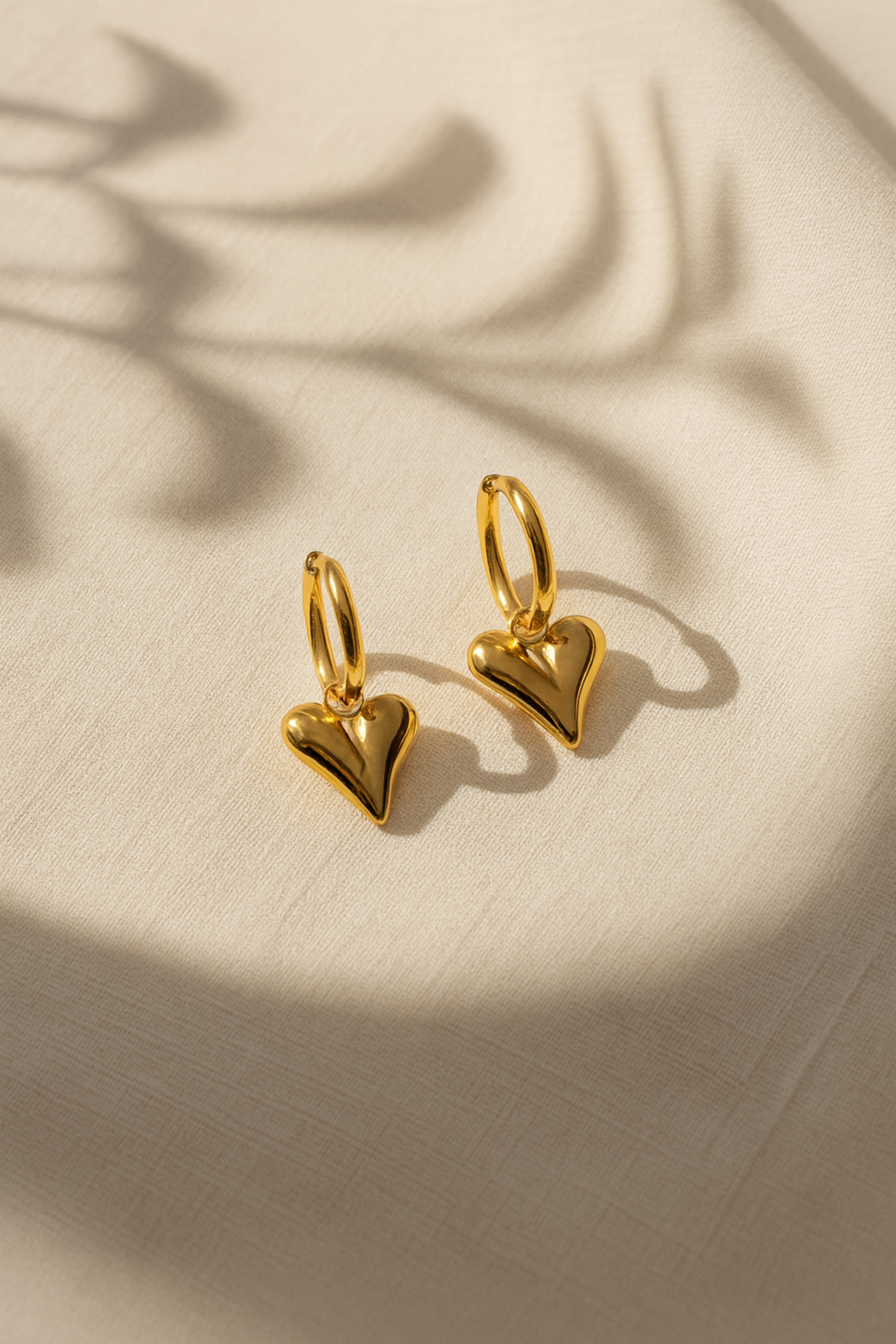 Gold heart-shaped earrings on a beige fabric background