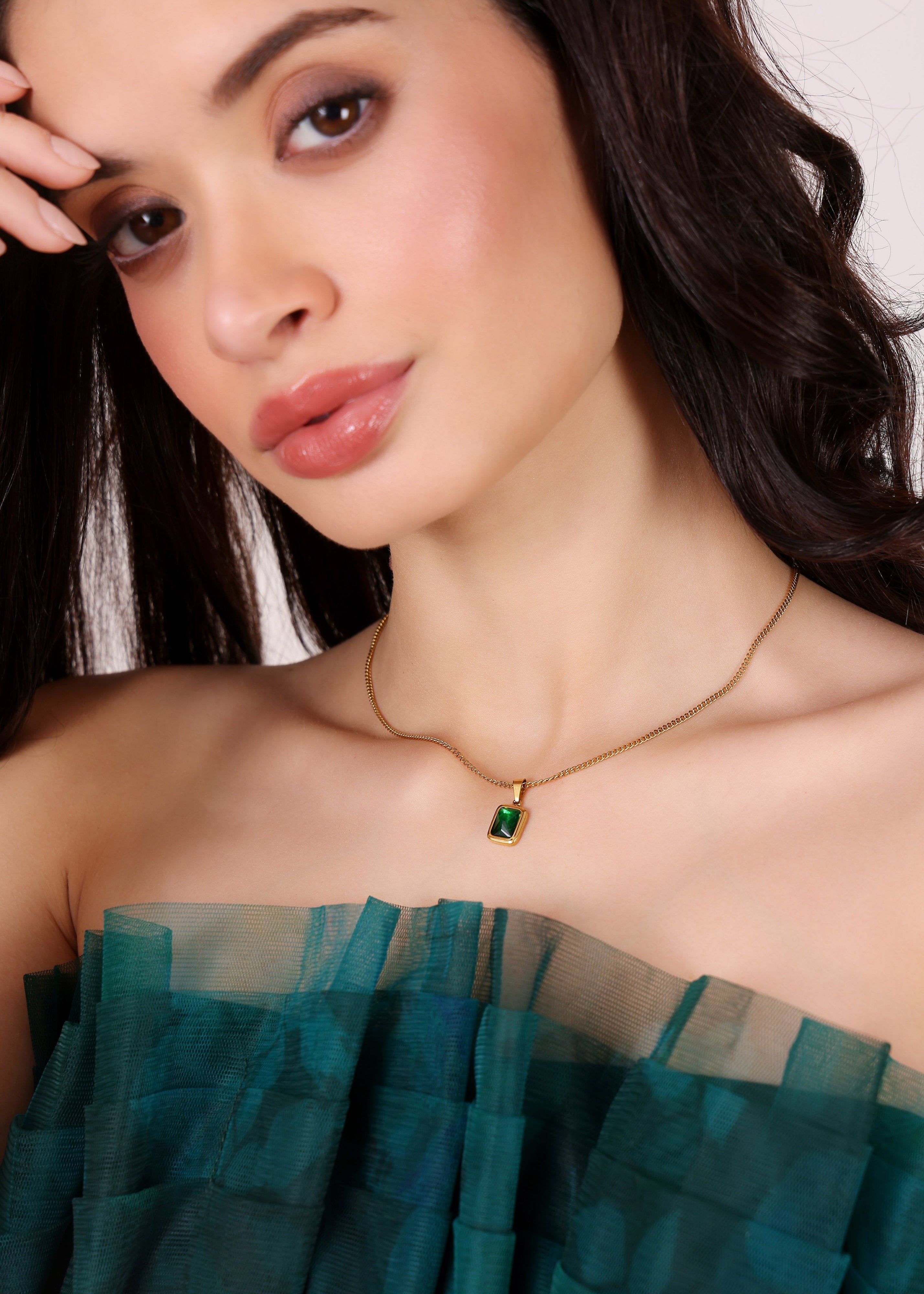 Woman wearing a green dress and gold necklace with a green gemstone.
