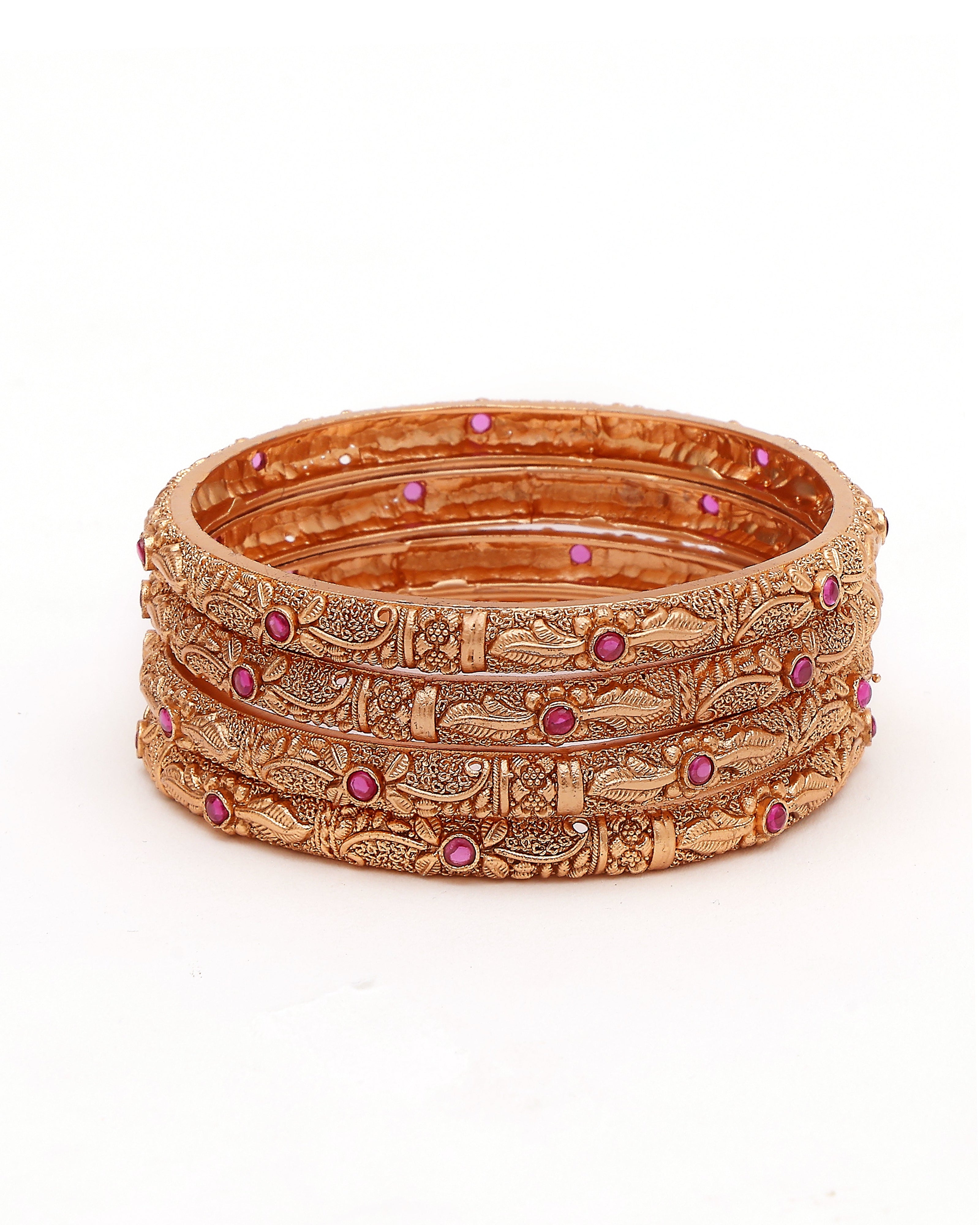 Set of ornate gold bangles with red stones on a white background