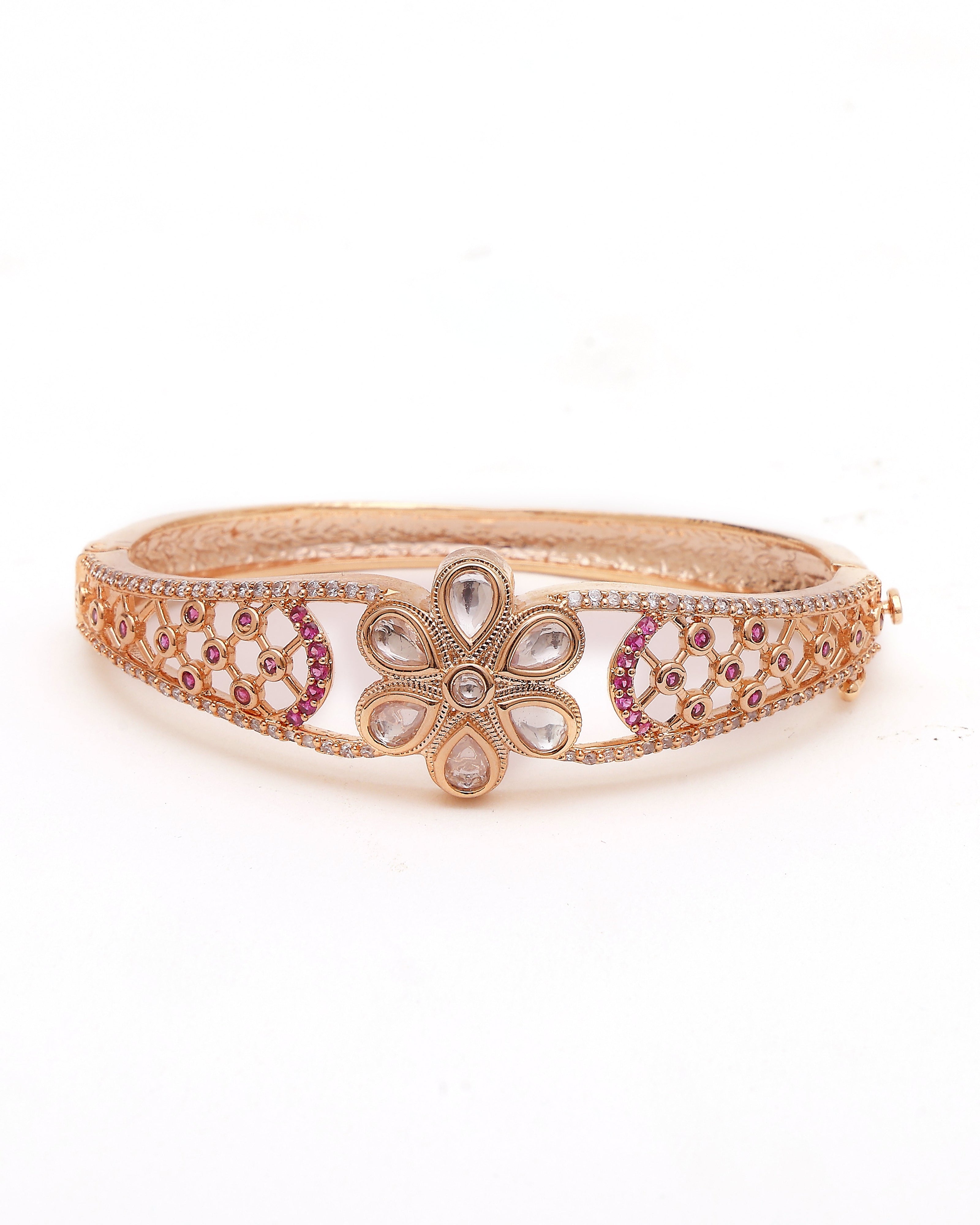 Decorative bangle with floral design and pink stones on a white background