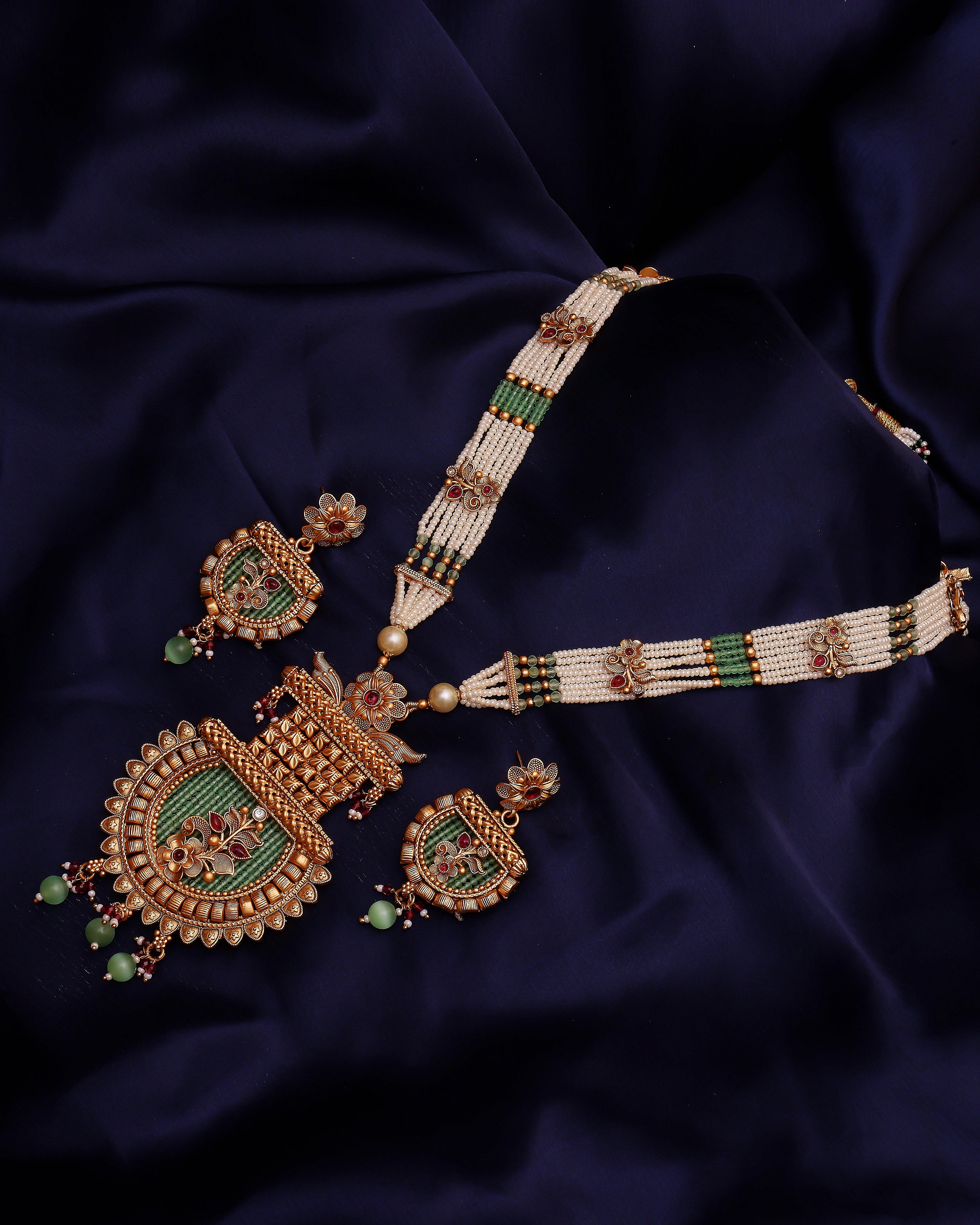 Ornate gold and green jewelry set on a dark blue fabric background