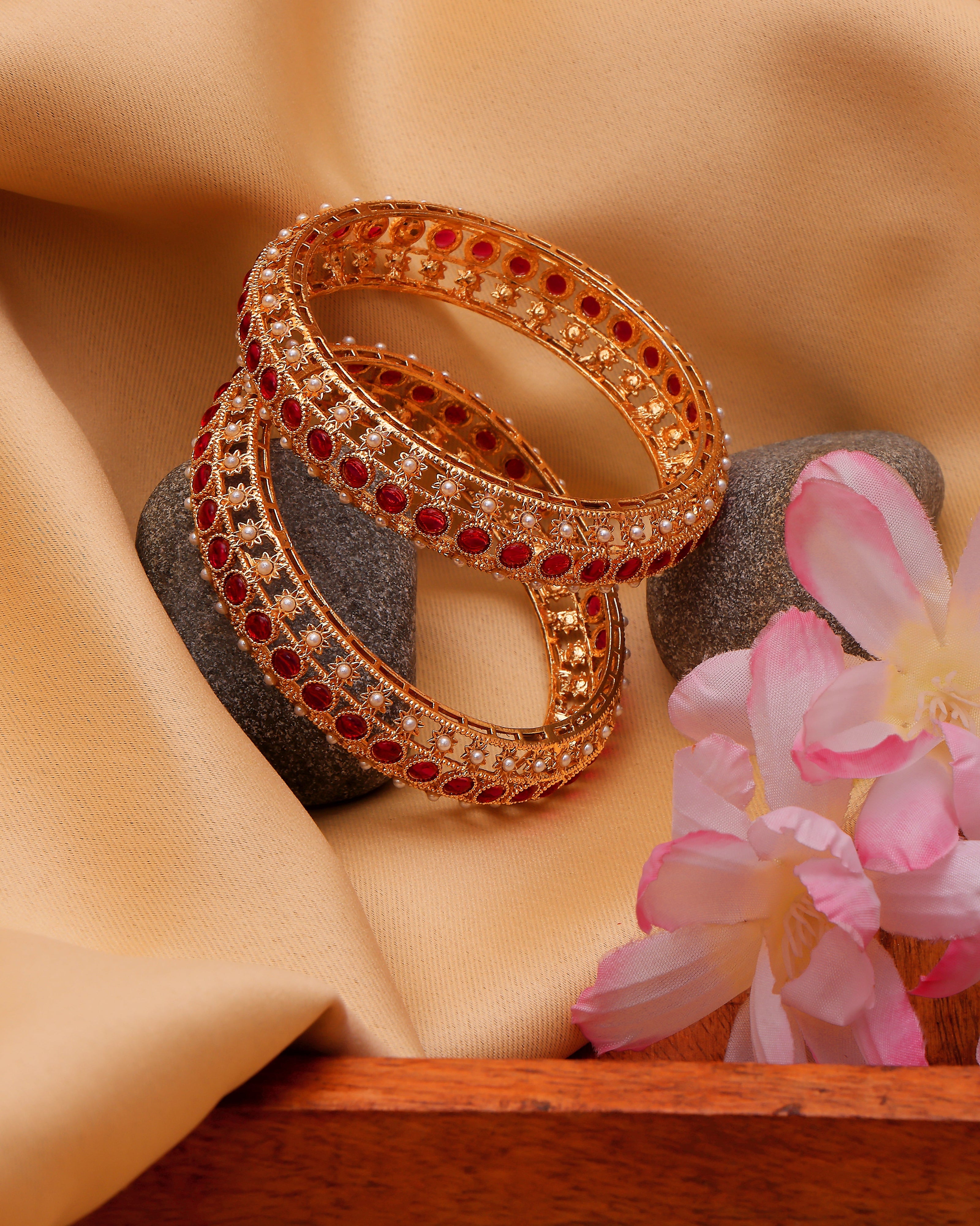 Gold bangles with red stones on a beige fabric background with flowers