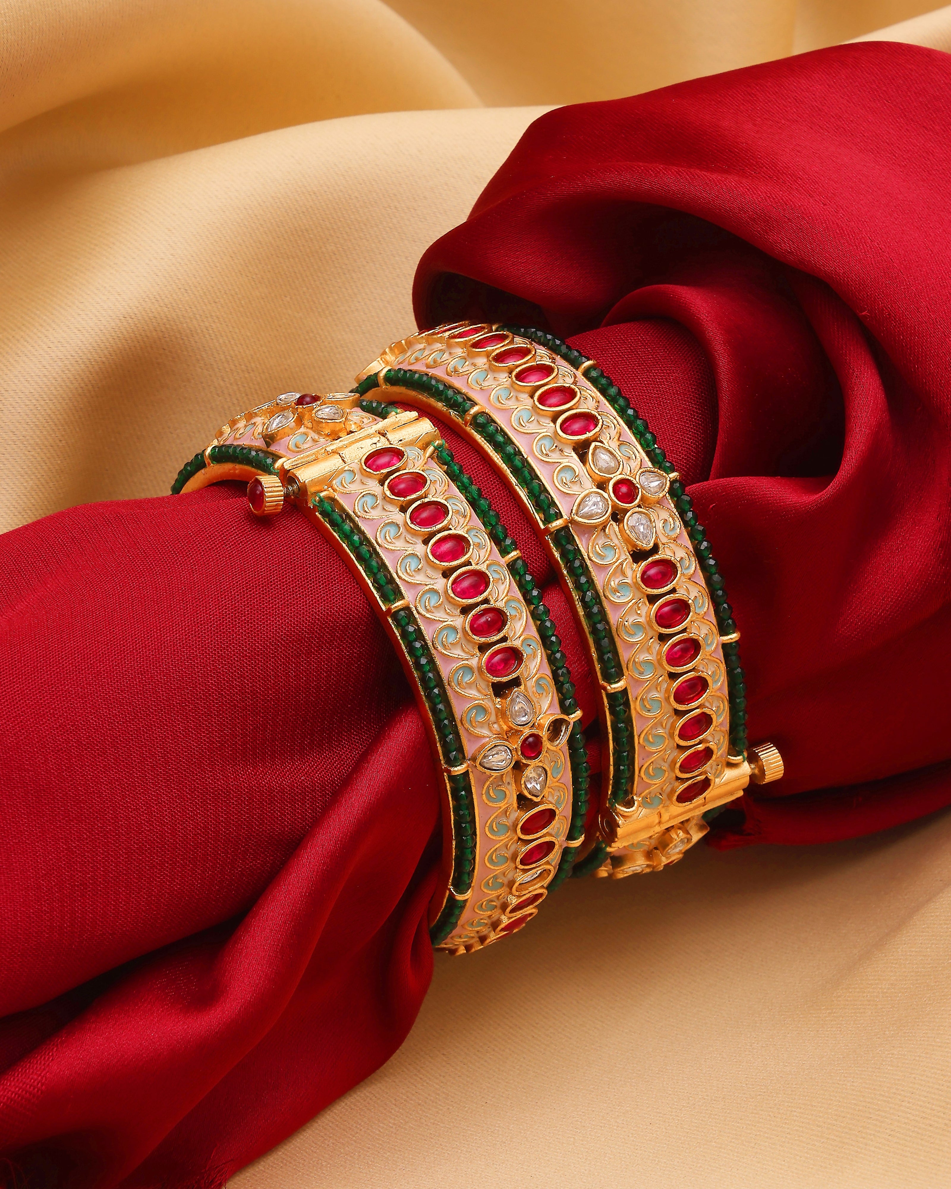 Gold and green bangles with red stones on a red fabric background