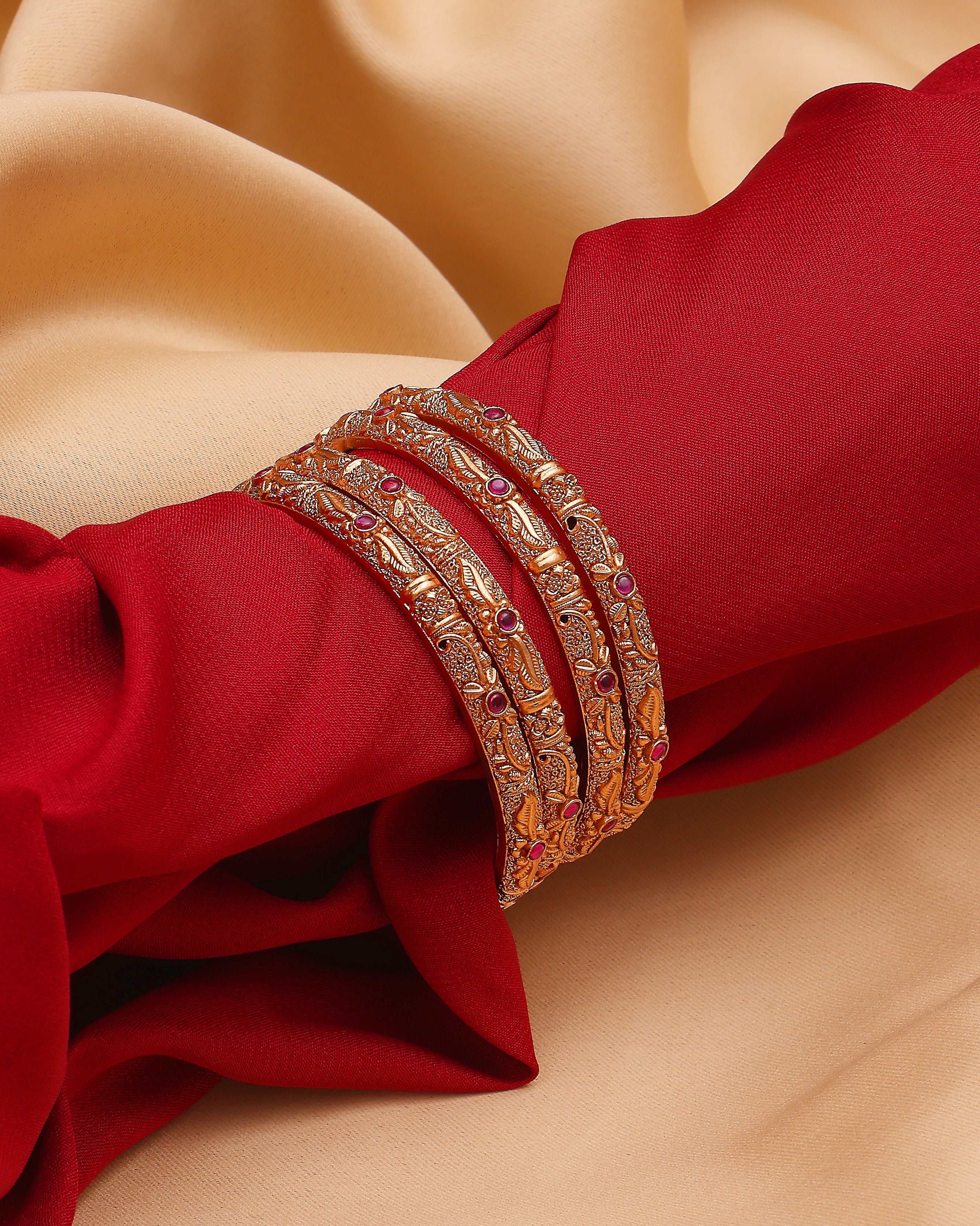 Gold bangles with red stones on a red fabric background