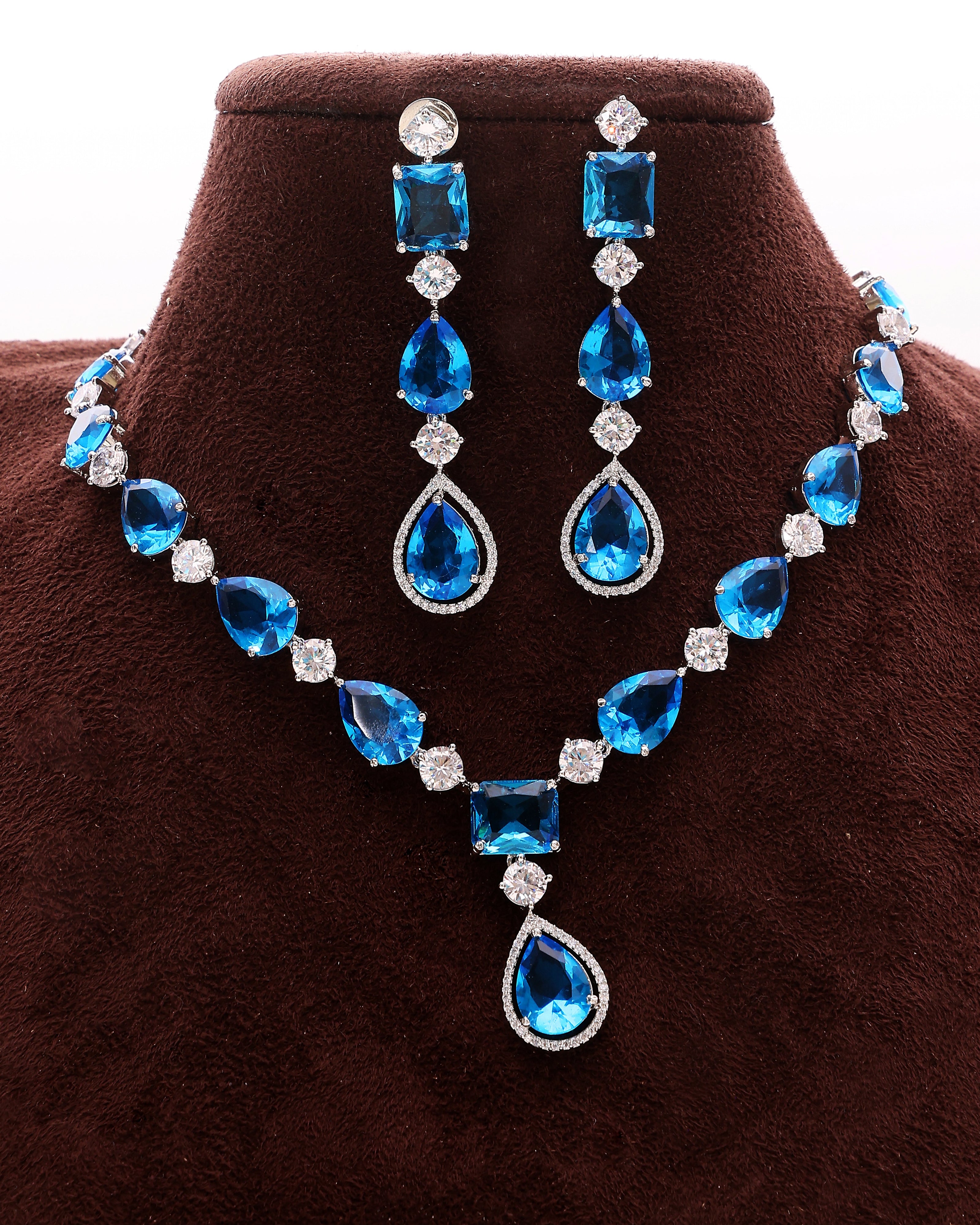 Blue teardrop necklace and earrings set on a brown velvet stand