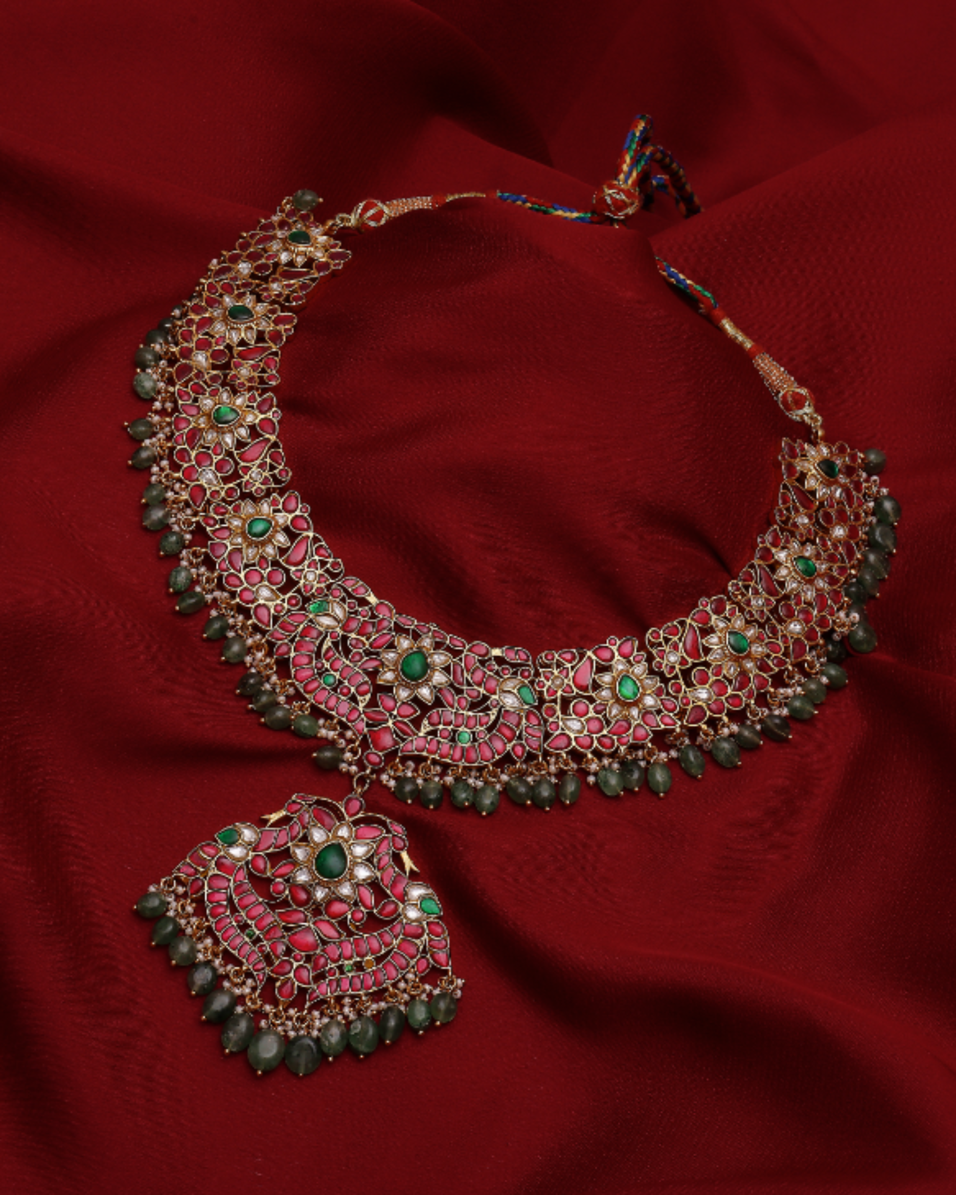 Ornate necklace with green and red stones on a red fabric background