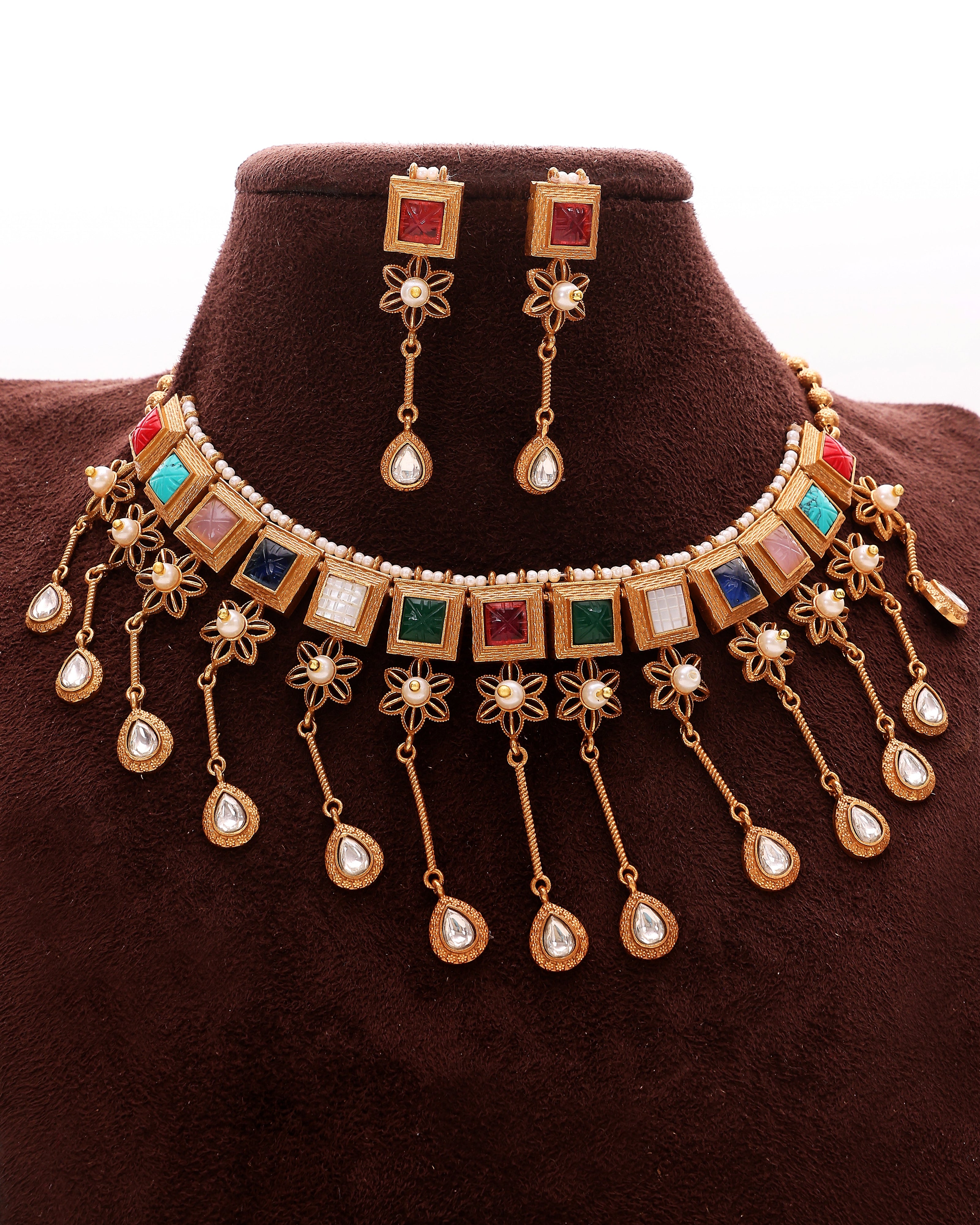 Gold necklace and earrings with colorful stones on a brown velvet stand