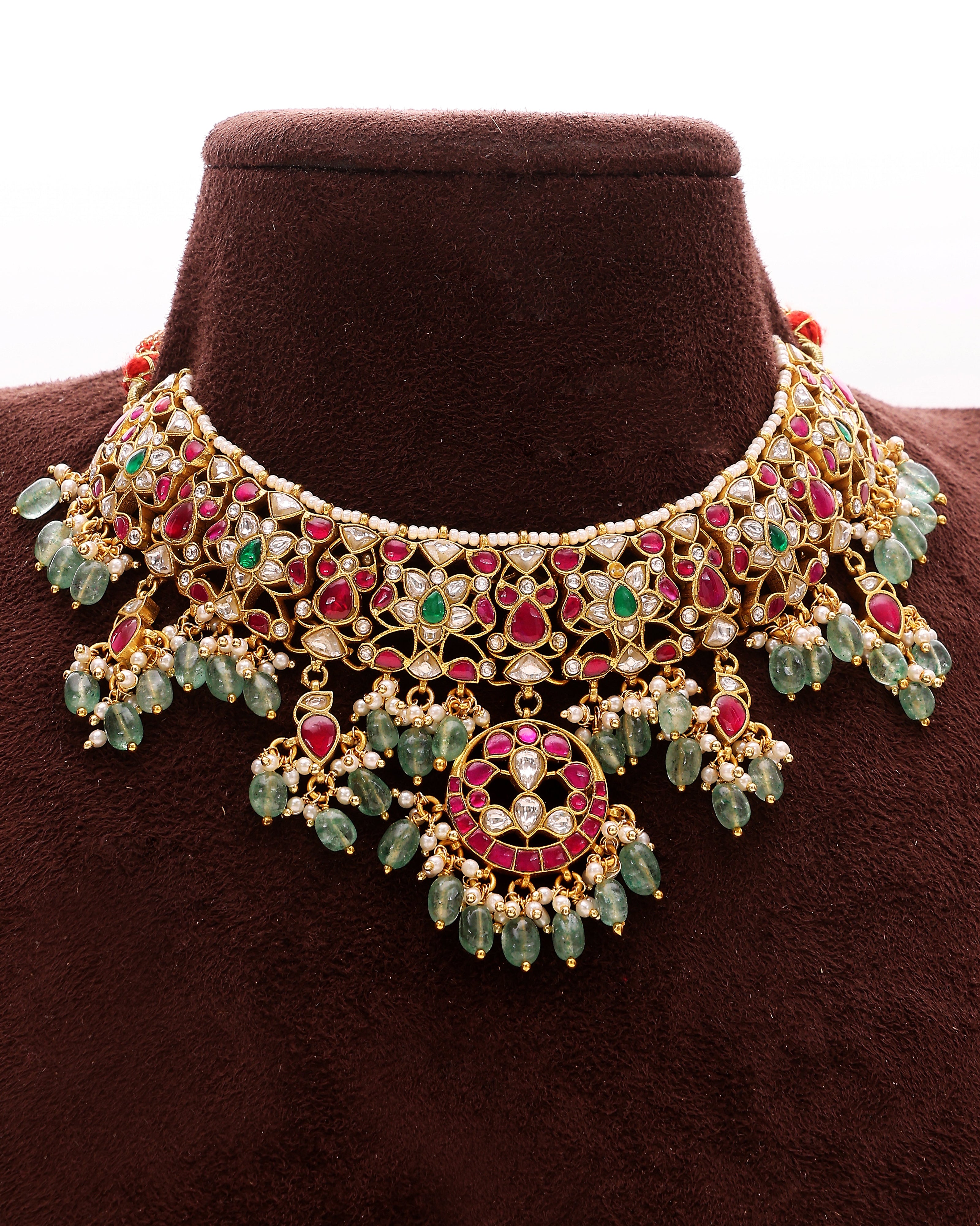 Ornate necklace with green and red stones on a brown mannequin
