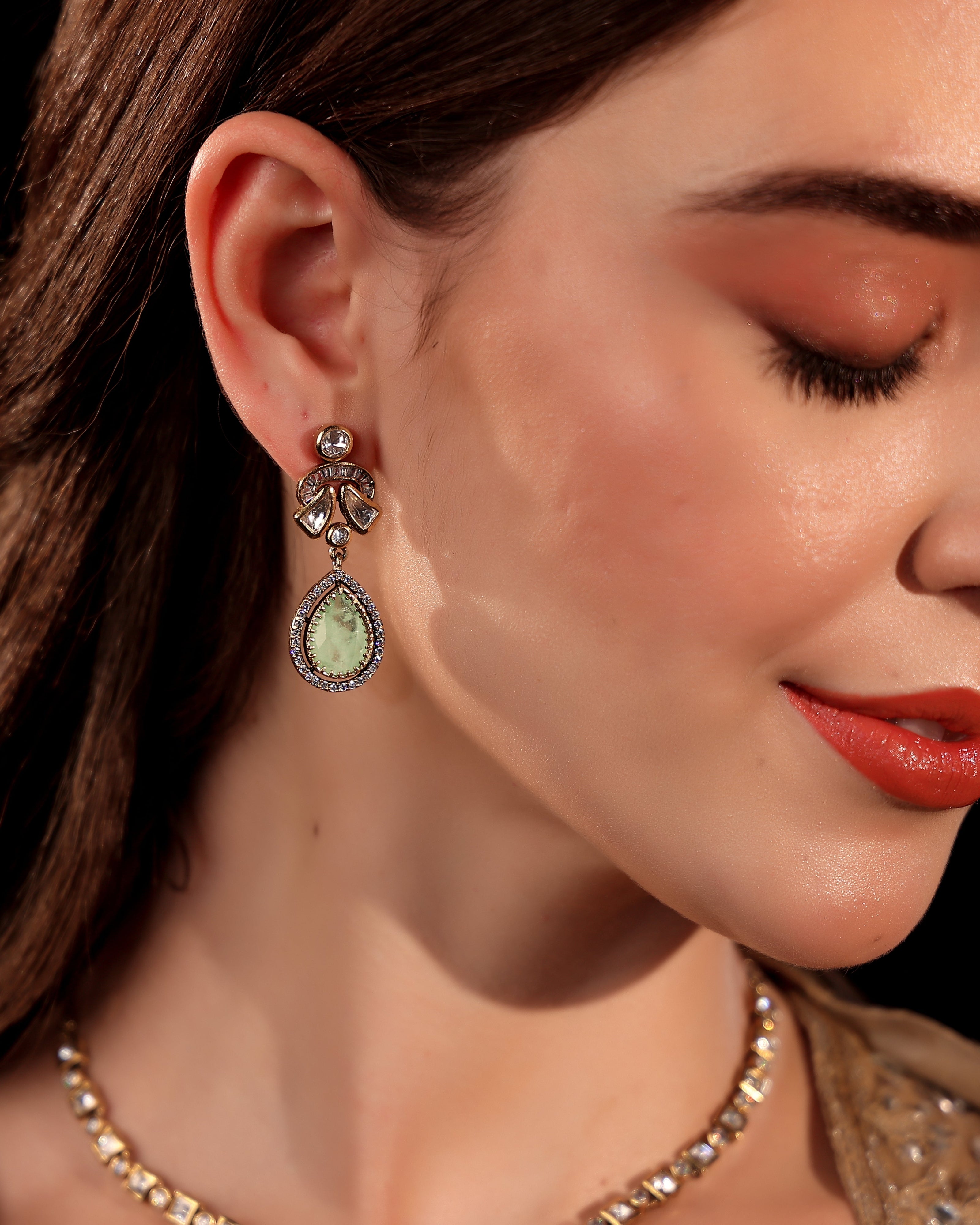 Close-up of a woman wearing a green teardrop earring with a blurred background