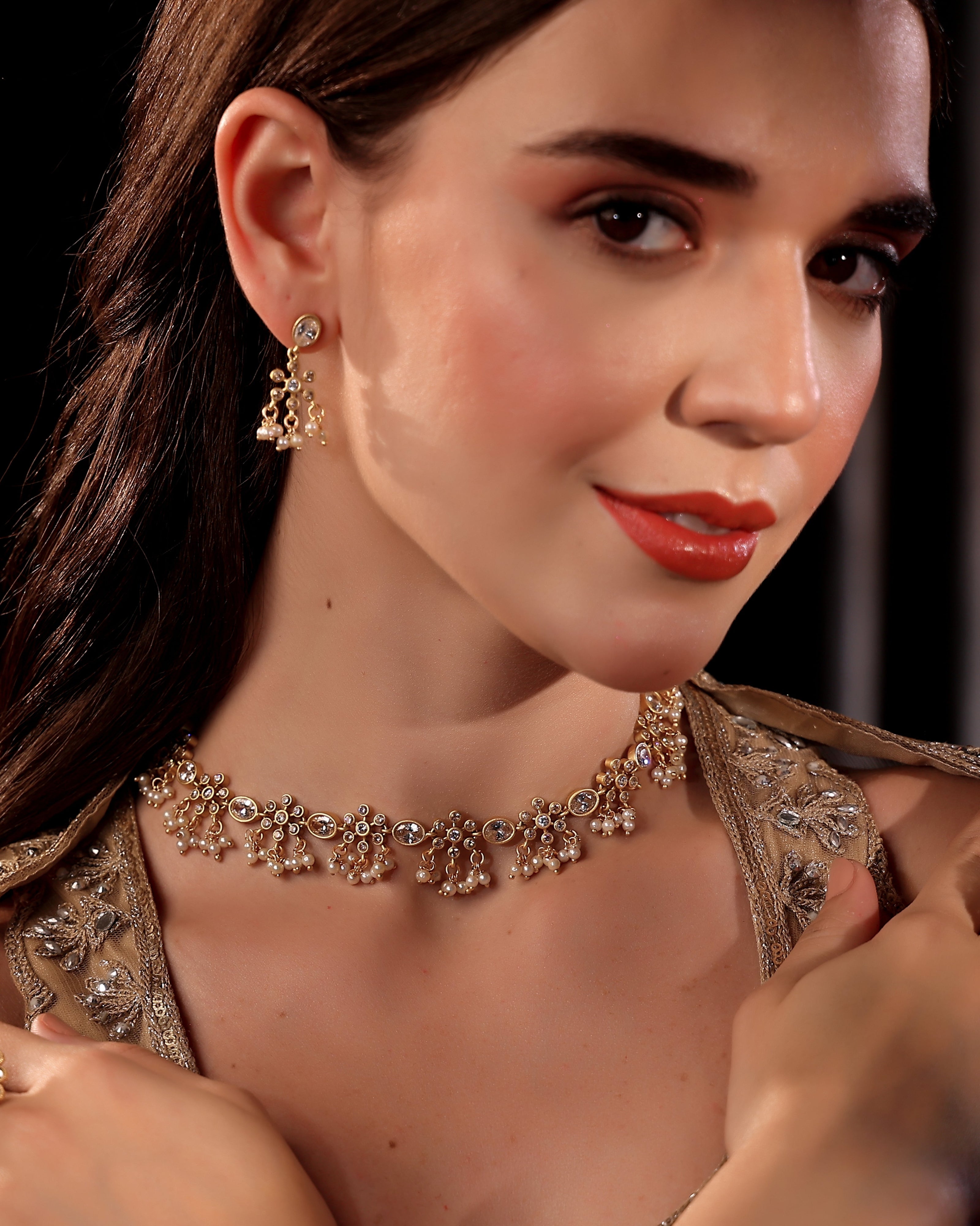 Woman wearing a gold necklace and earrings with a dark background