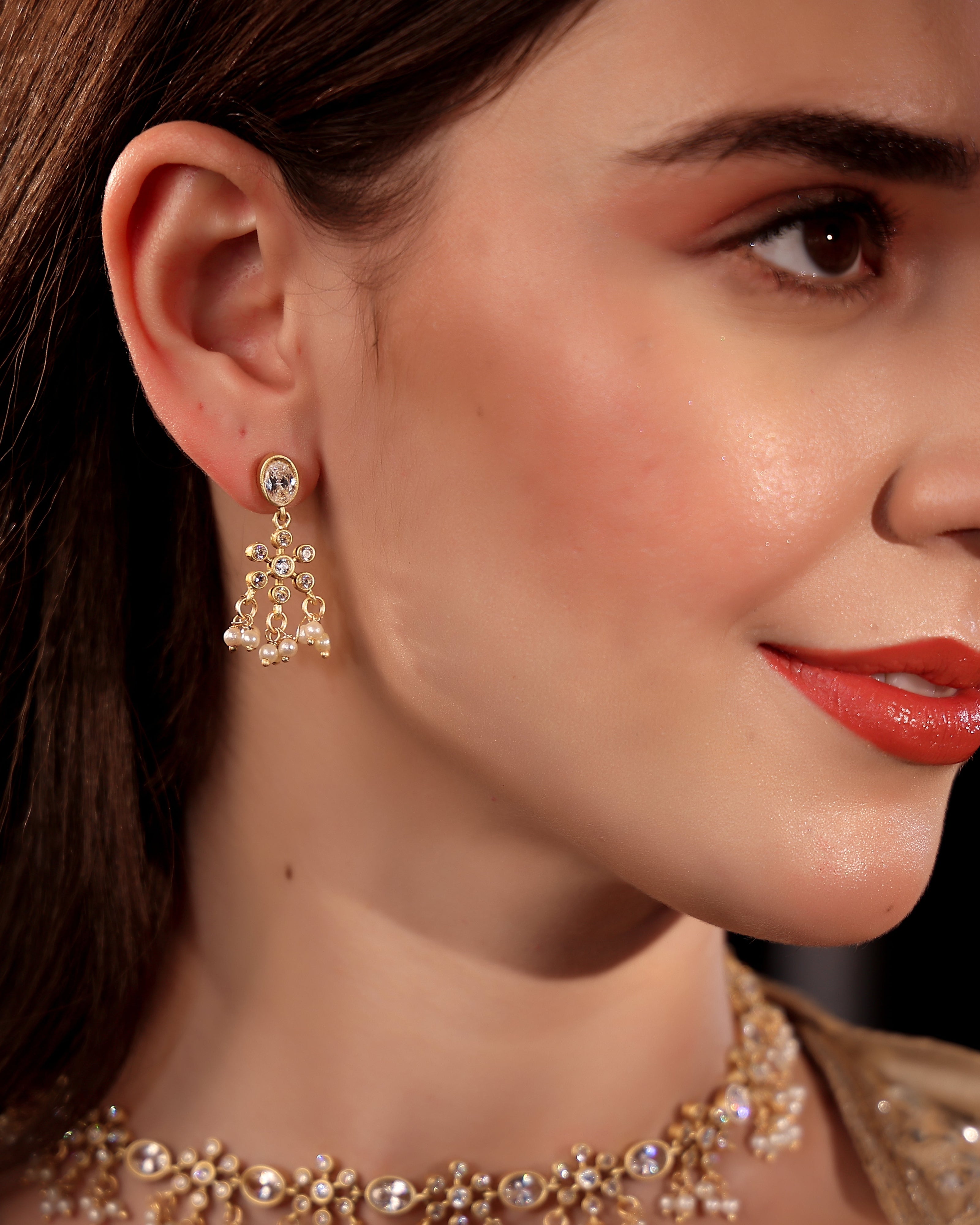 Close-up of a woman wearing gold earrings and a necklace with a blurred background