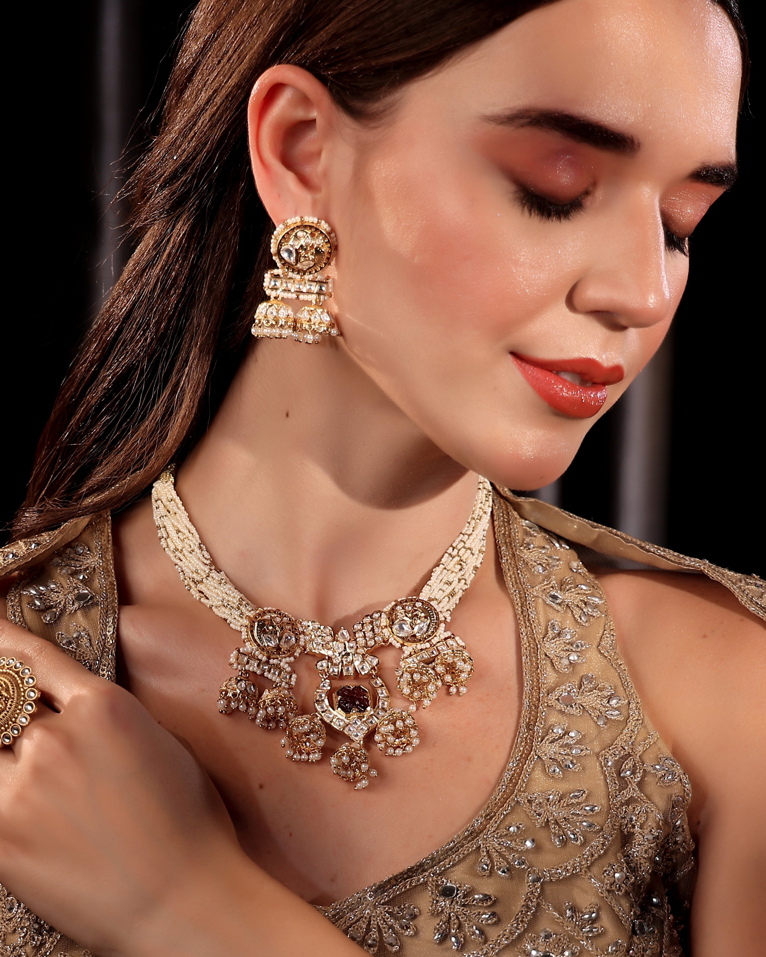 Woman wearing gold jewelry including earrings and a necklace against a dark background