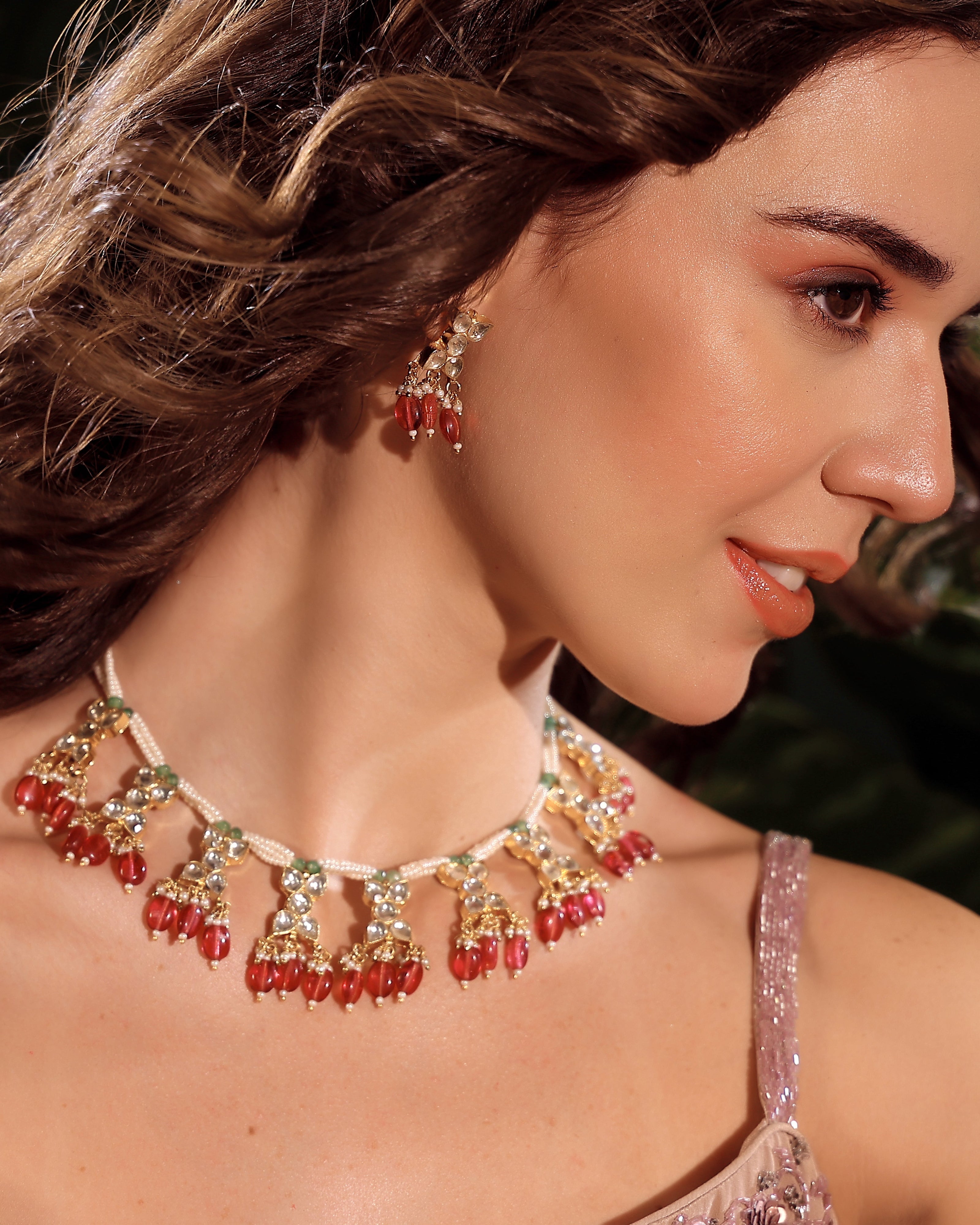 Woman wearing a red and gold necklace with matching earrings.