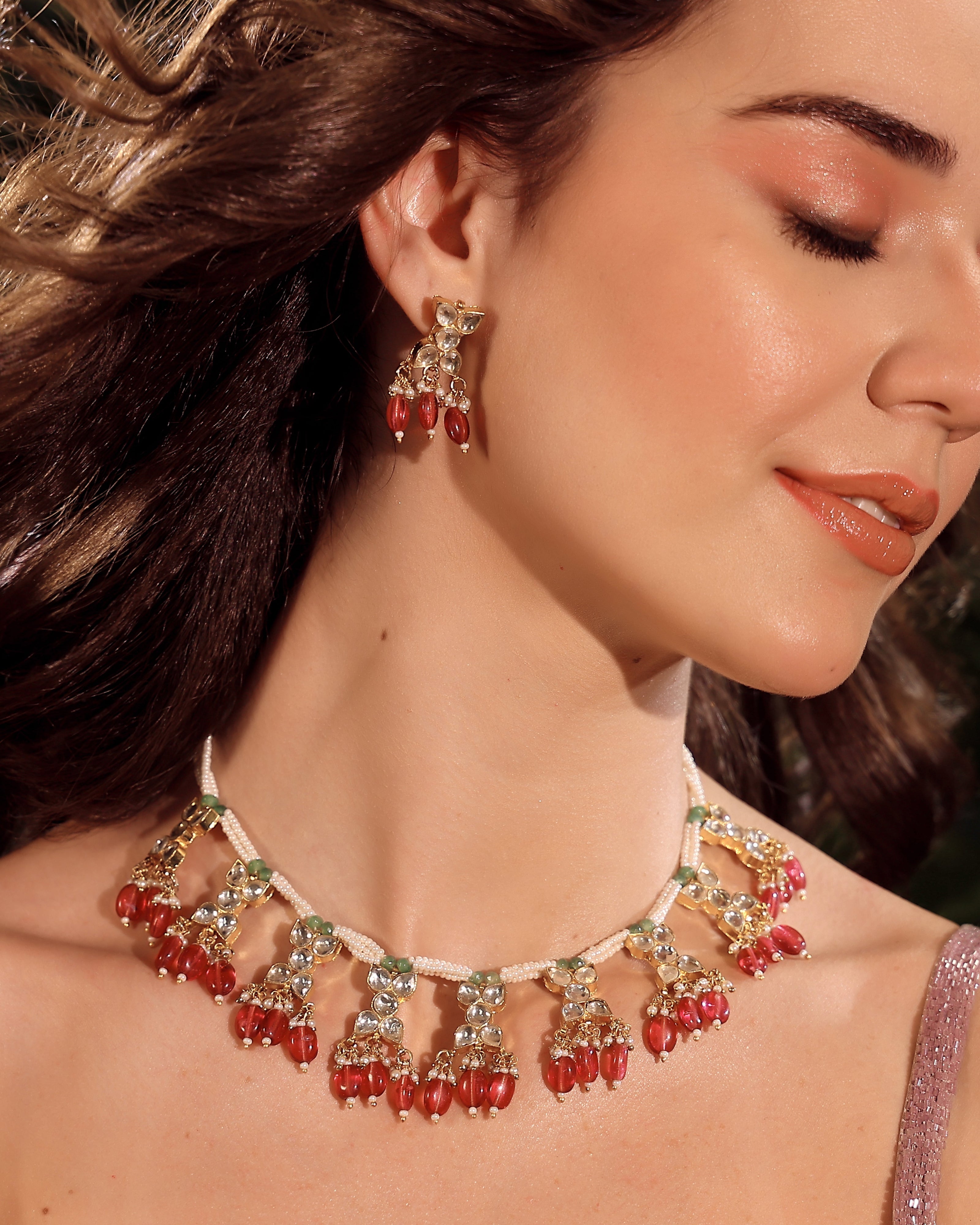 Woman wearing a red and gold necklace with matching earrings.